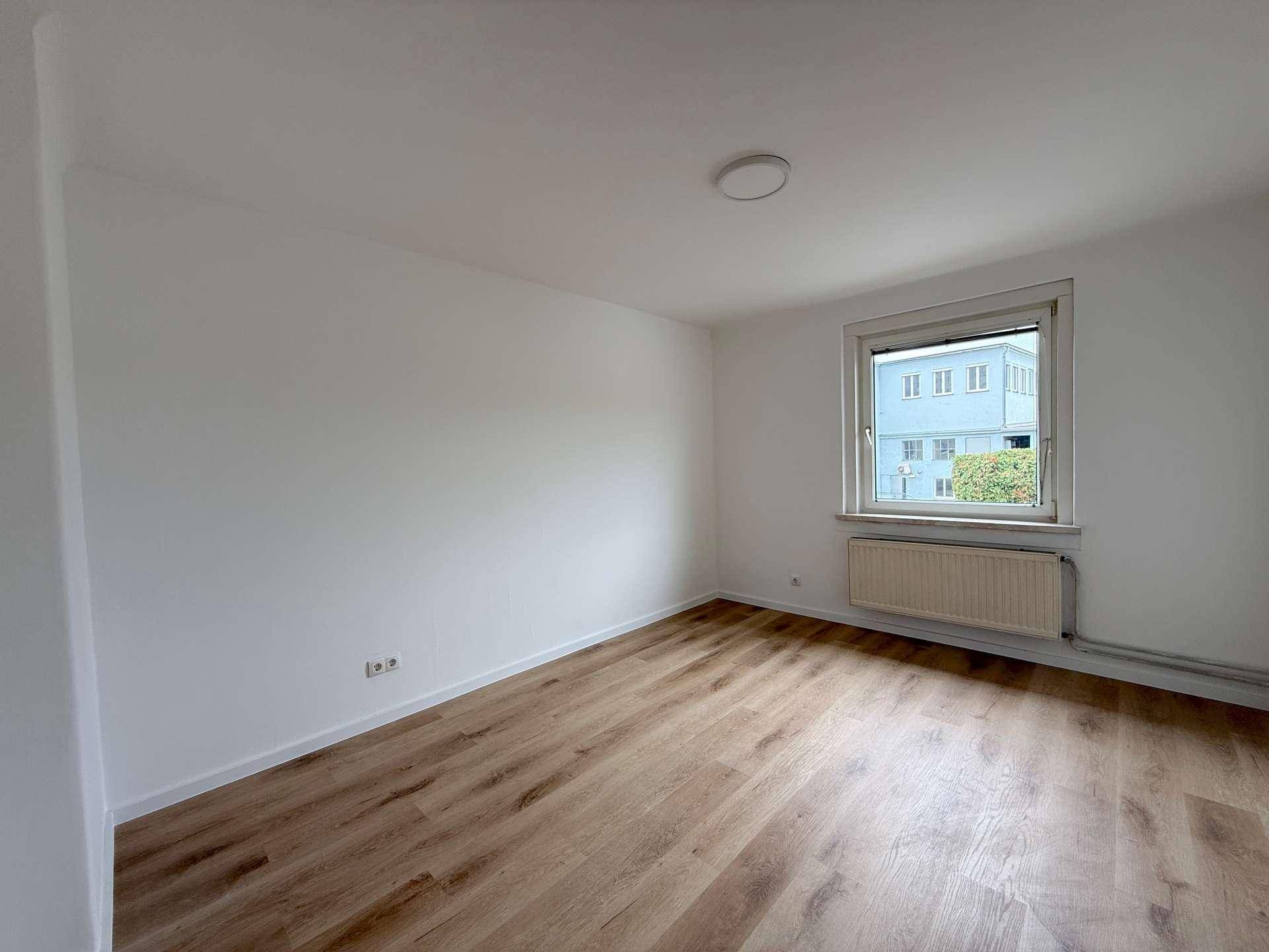 Helles Zimmer mit Laminatboden, weißen Wänden und einem Fenster mit Blick auf die Umgebung.