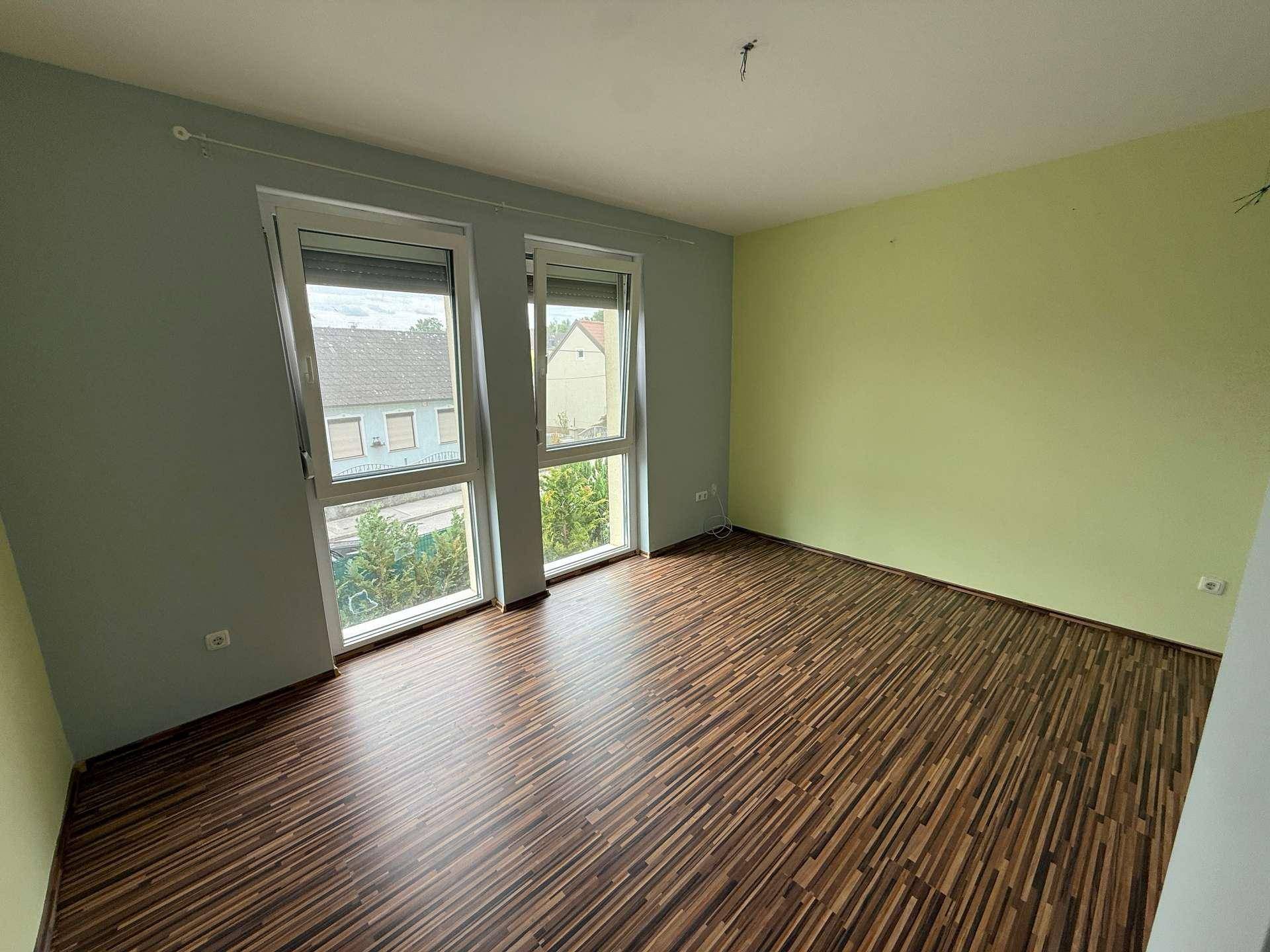 Schlafzimmer mit Laminatboden, großen Fenstern und farbigen Wänden in Grün und Grau.