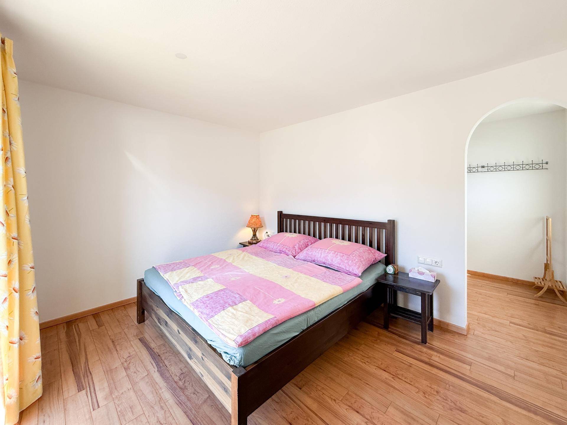 Helles Schlafzimmer mit Holzboden und einem Durchgang zu einem weiteren Bereich.