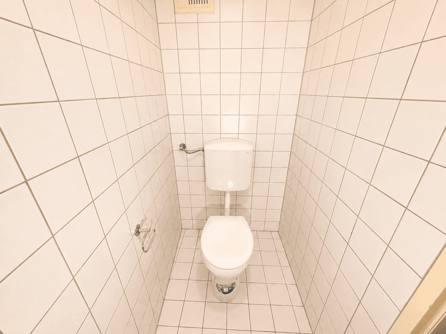 Kleines WC mit weißen Fliesen an Wänden und Boden, ausgestattet mit einer Toilette.