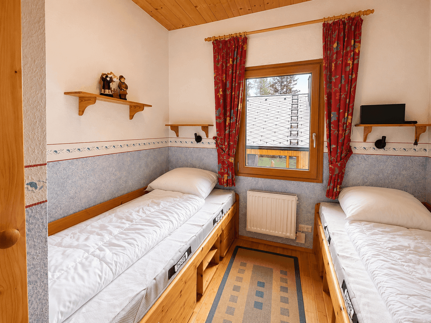 Schlafzimmer mit zwei Einzelbetten, Holzfenster und farbiger Tapete.