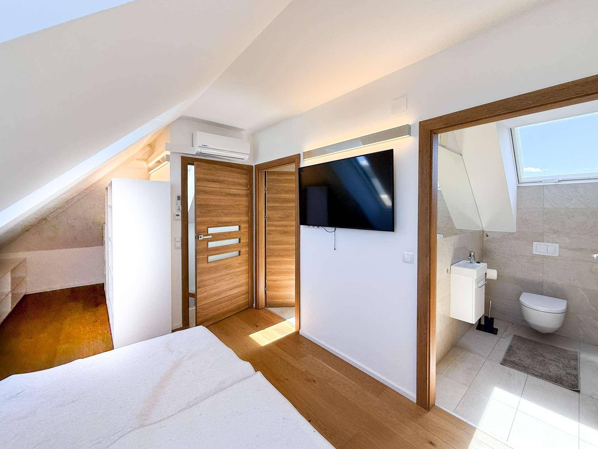 Schlafzimmer mit Wandfernseher, Klimaanlage und direktem Zugang zu einem angrenzenden Badezimmer.