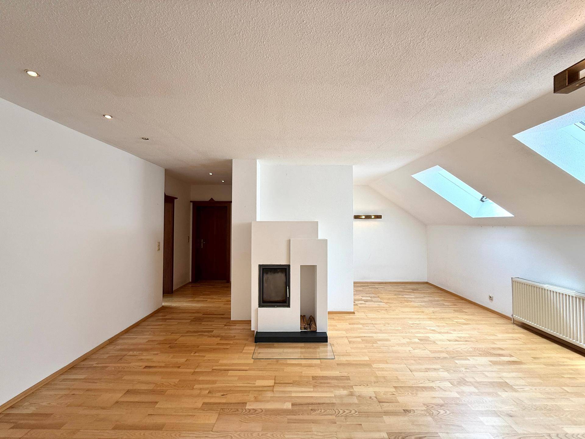 Helles Wohnzimmer im Dachgeschoss mit modernem Kamin, Holzboden und zwei Dachfenstern.