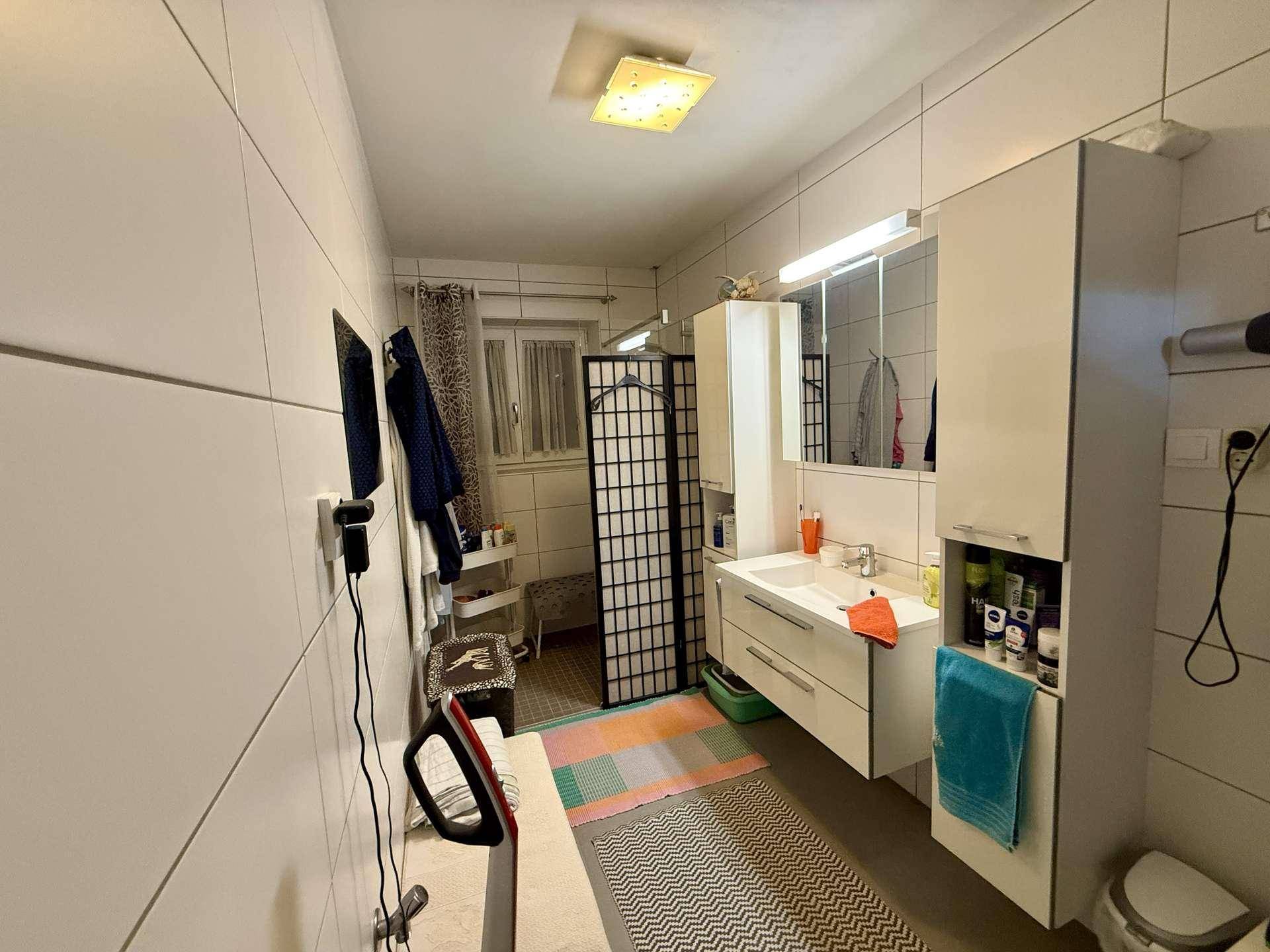 Helles Badezimmer mit Doppelwaschbecken, Spiegelschrank und Fenster.