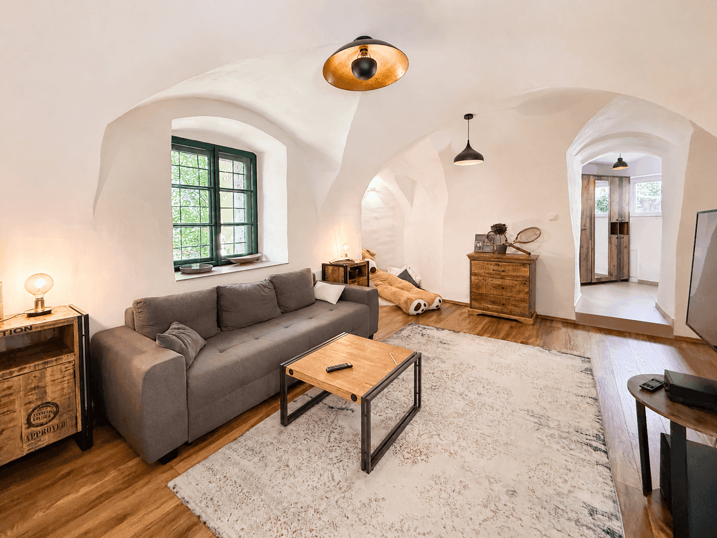 Heller Wohnbereich mit bequemer Couch, Holzboden und rustikalen Möbeln unter Gewölbedecken.
