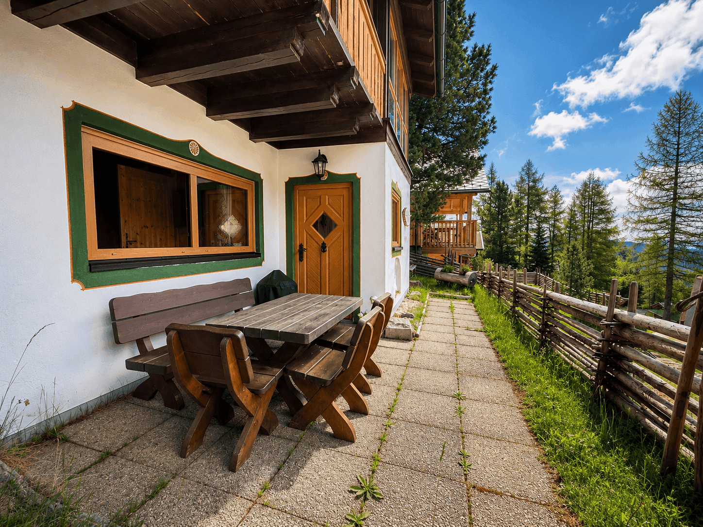 Gemütliche Terrasse mit Holztisch und Bänken vor dem Chalet, umgeben von Natur und Zaun.