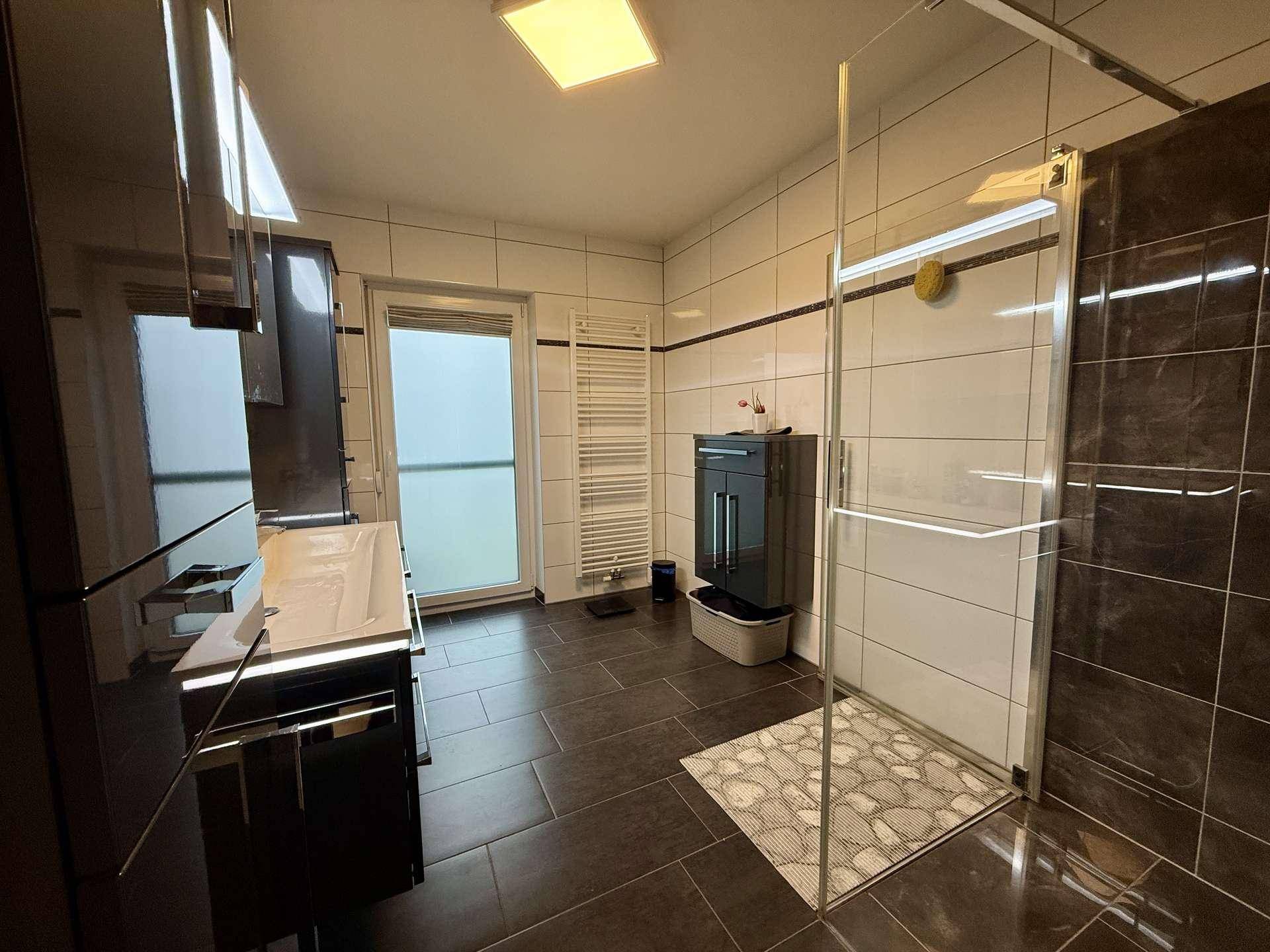 Modernes Badezimmer mit großer begehbarer Dusche, dunklen Fliesen und Fenster.