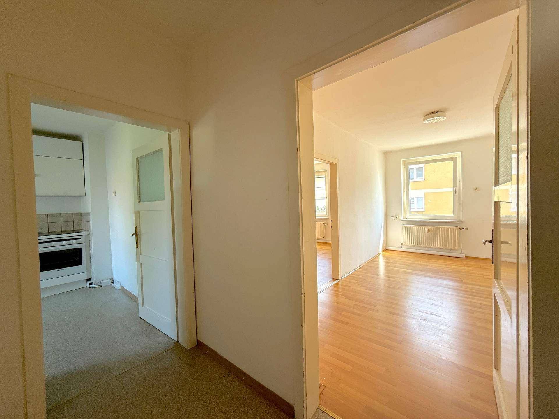 Heller Flur mit Zugang zu einer Küche und einem weiteren Zimmer mit Parkettboden und Fenster.
