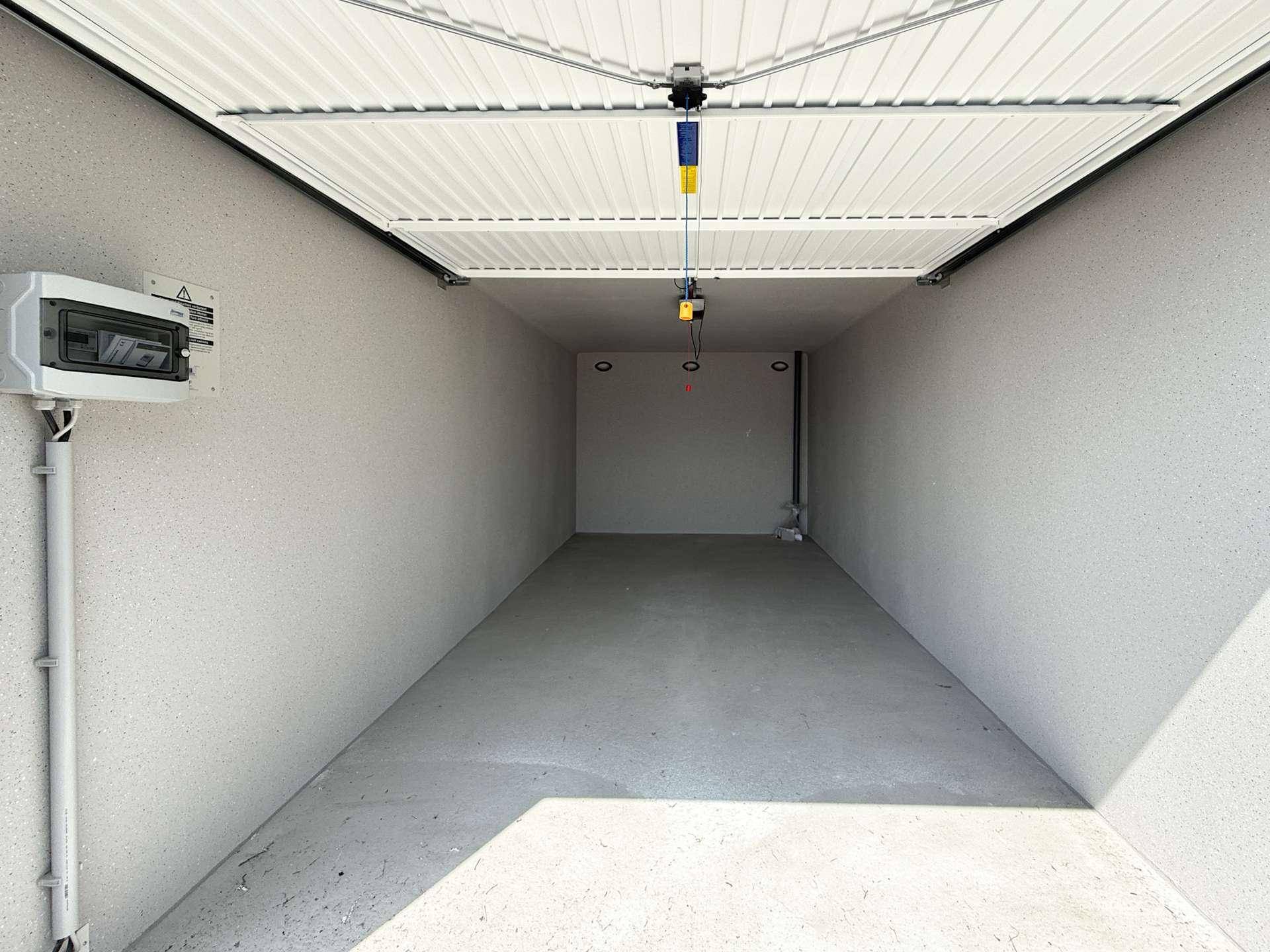Leere, saubere Garagenbox mit Betonboden und einem elektrischen Schaltkasten an der Wand.