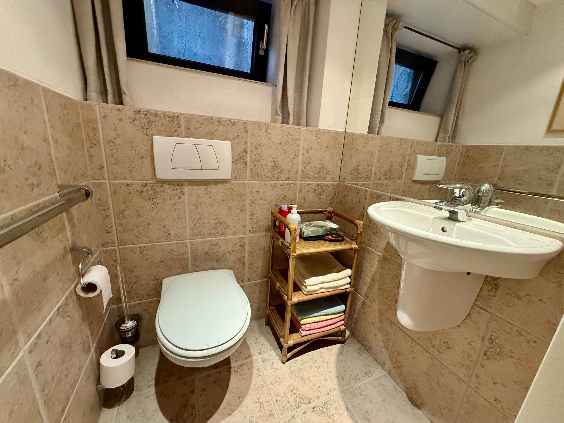 Kleines Gäste-WC mit Wand-WC, Einzelwaschbecken und beigefarbenen Fliesen.