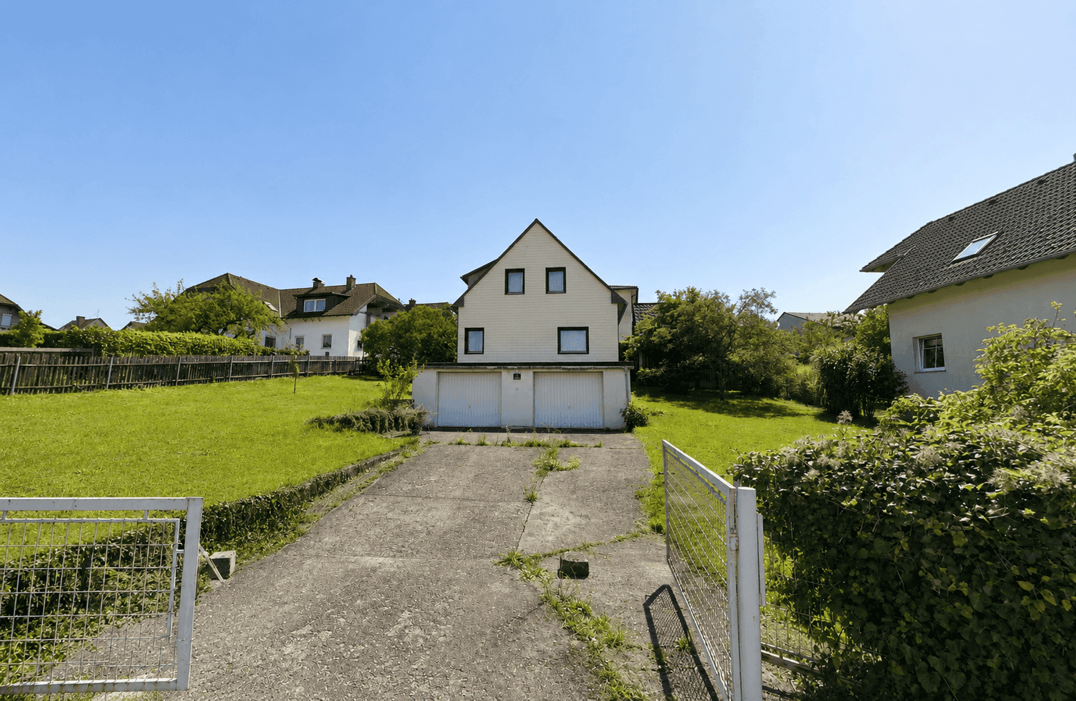 Einfamilienhaus mit Doppelgarage und Zufahrt, umgeben von Grünflächen an einem sonnigen Tag.
