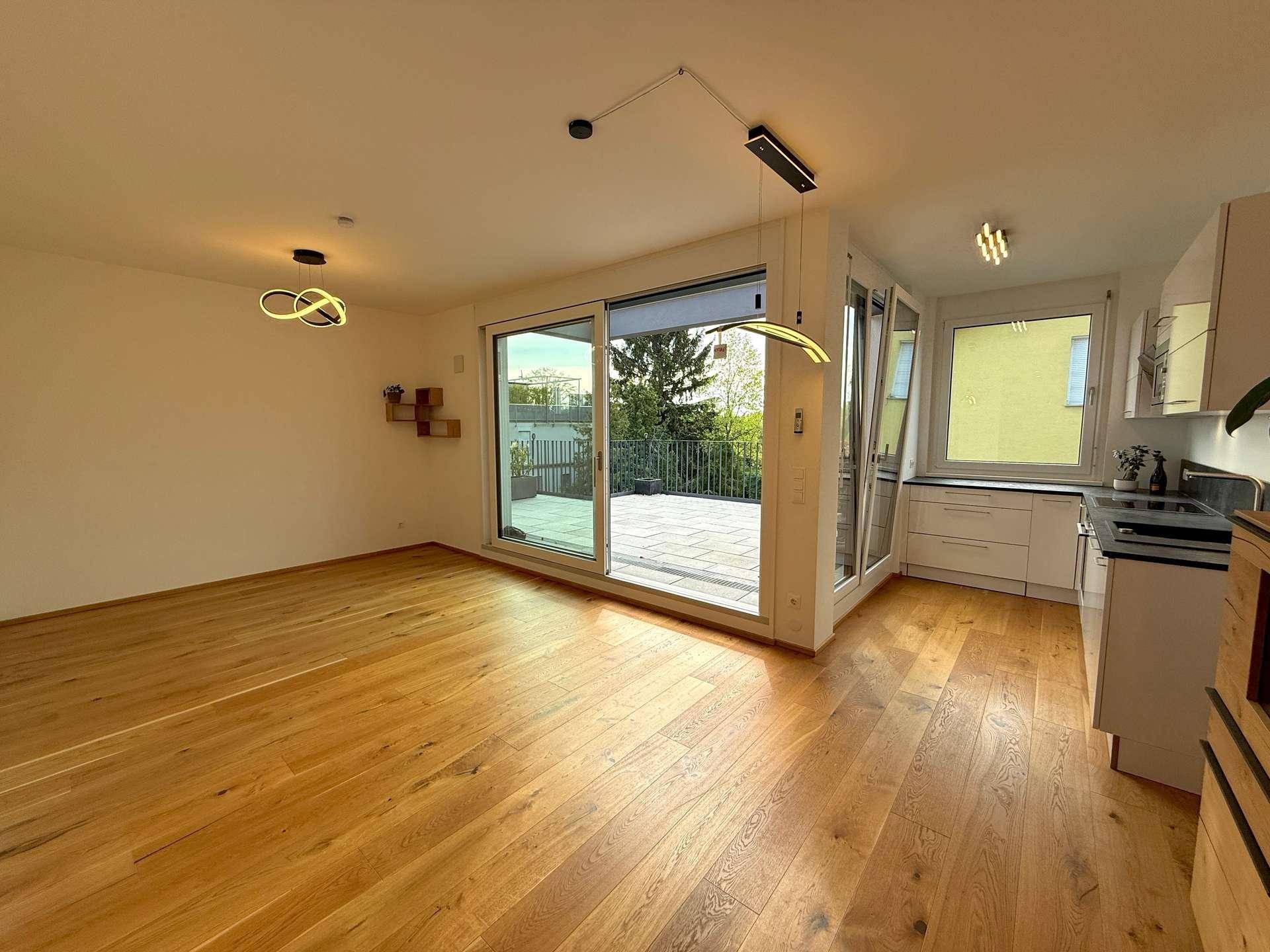 Heller offener Wohn-Essbereich mit Holzboden und Zugang zu einer großen Terrasse.