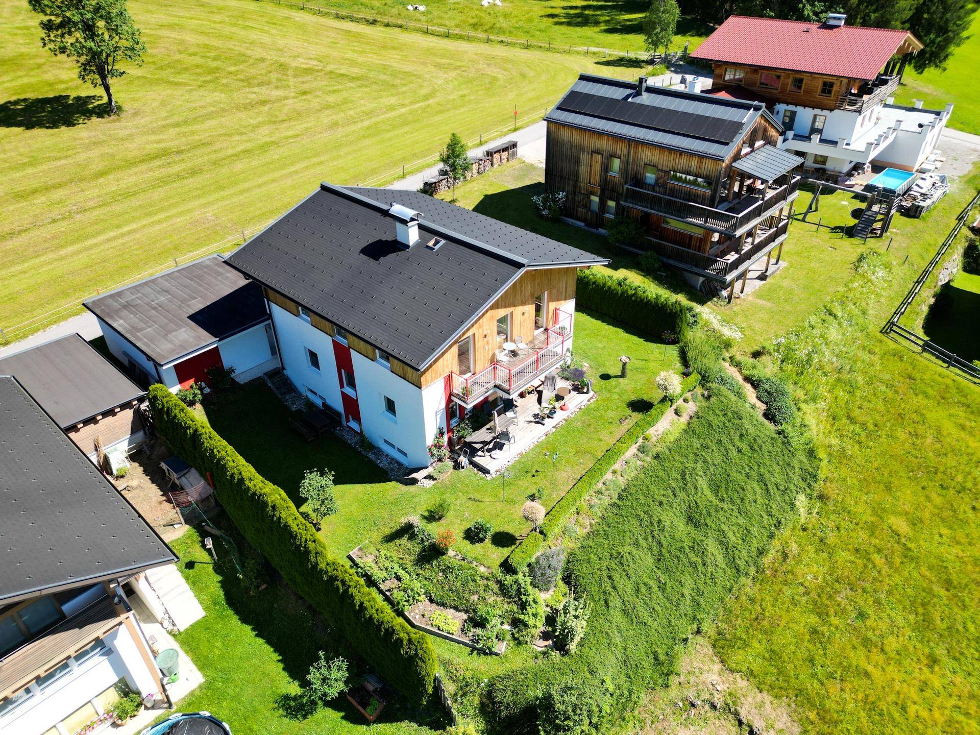 Vogelperspektive des Hauses mit Garten, umgeben von üppiger grüner Vegetation und Bergen.