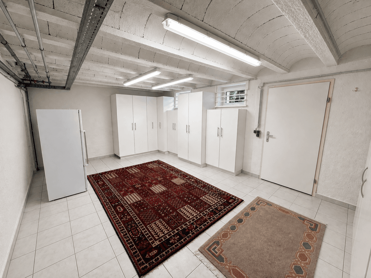 Geräumiger Kellerraum mit Fliesenboden, Lagerschränken und Kühlschrank.