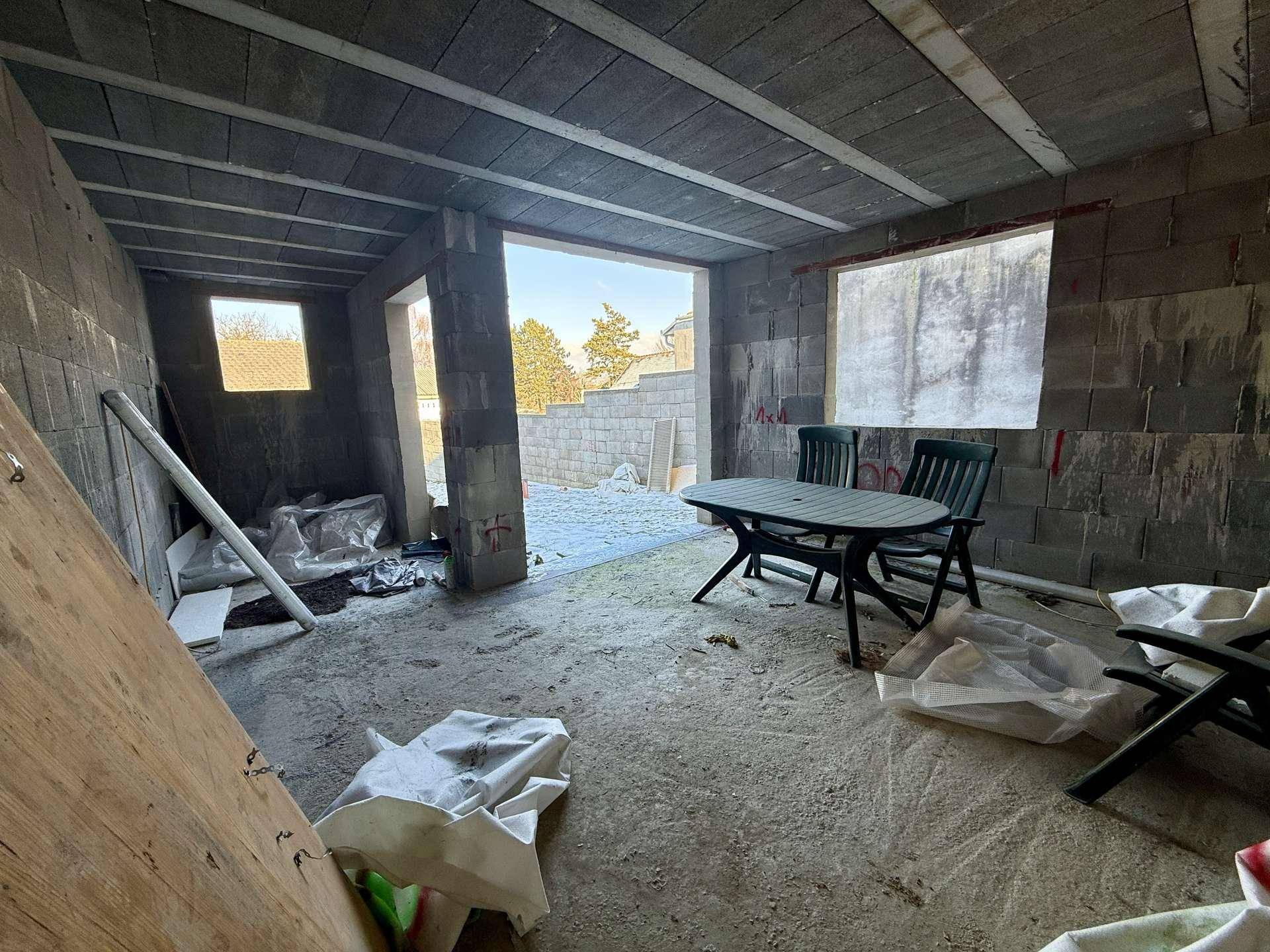 Innenansicht eines Rohbaus mit Betonwänden und -decke, offen zum Außenbereich.