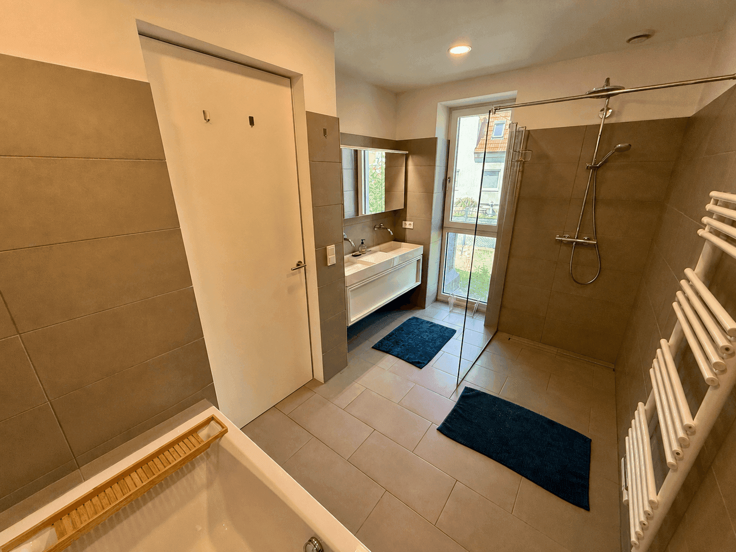Modernes Badezimmer mit Badewanne, ebenerdiger Dusche, Doppelwaschbecken und Fenster.