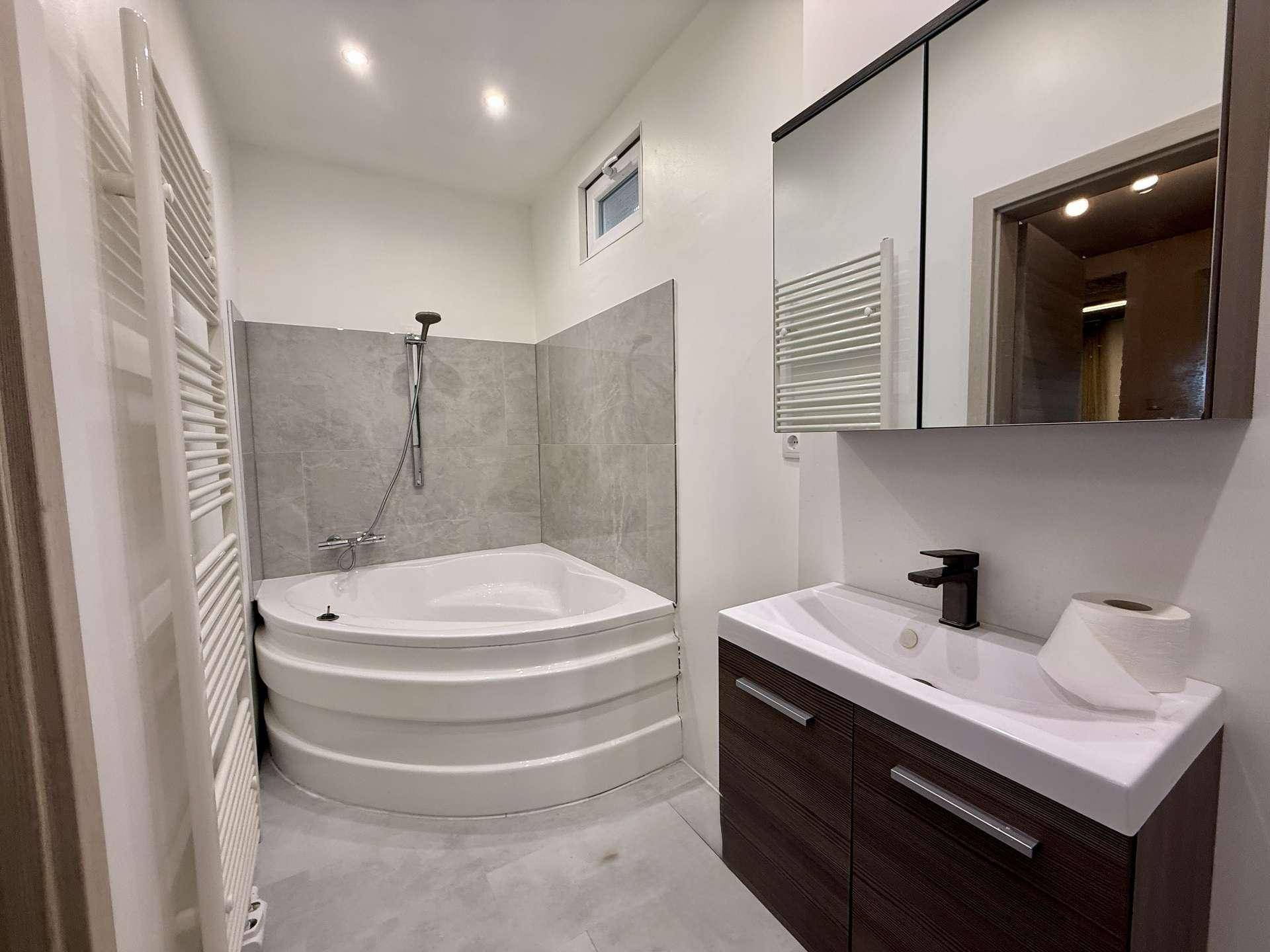 Modernes Badezimmer mit Eckbadewanne, Waschbecken und beheiztem Handtuchhalter.
