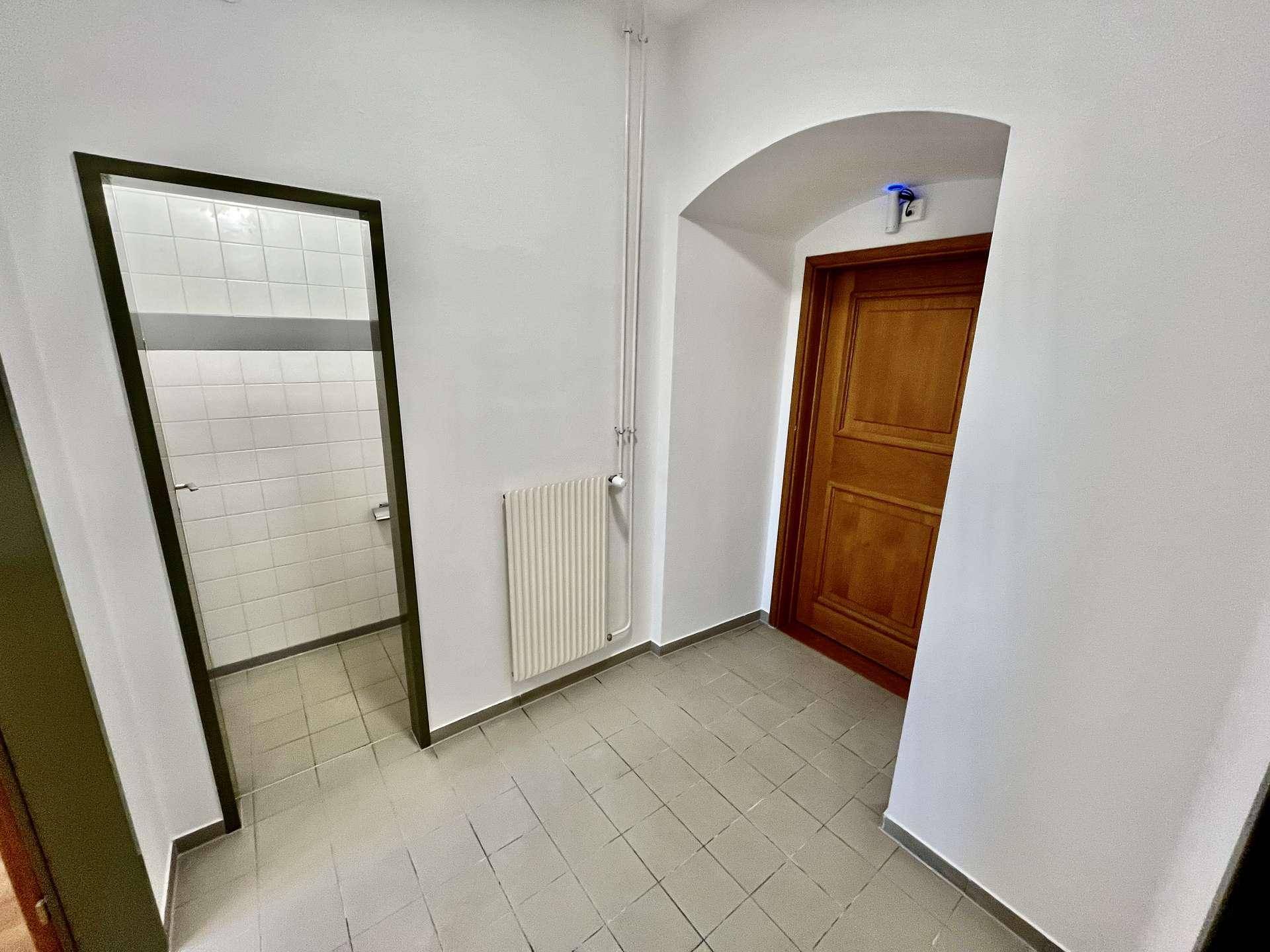 Flur mit Fliesenboden und Zugang zu einem Badezimmer mit weißen Fliesen an den Wänden.