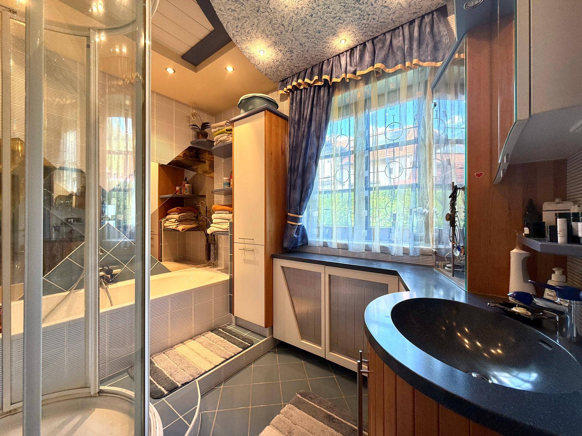 Badezimmer mit Dusche, Badewanne, Waschbecken und Fenster, ausgestattet mit blauen Fliesen.