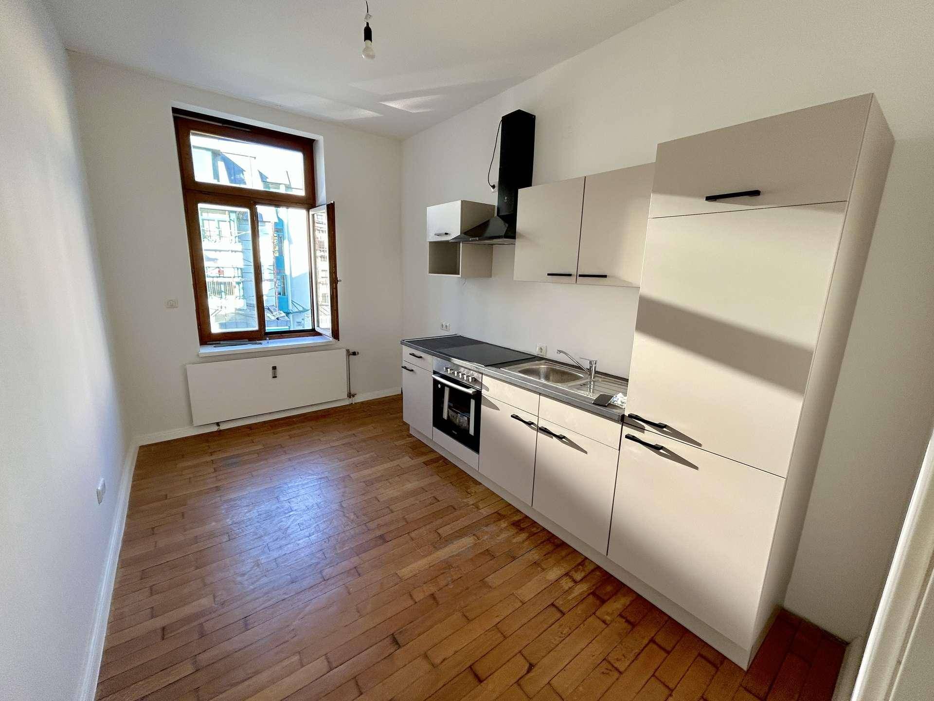 Kleine, funktionale Küche mit Einbauschränken, Herd und Spüle, ideal für eine kompakte Wohnung.
