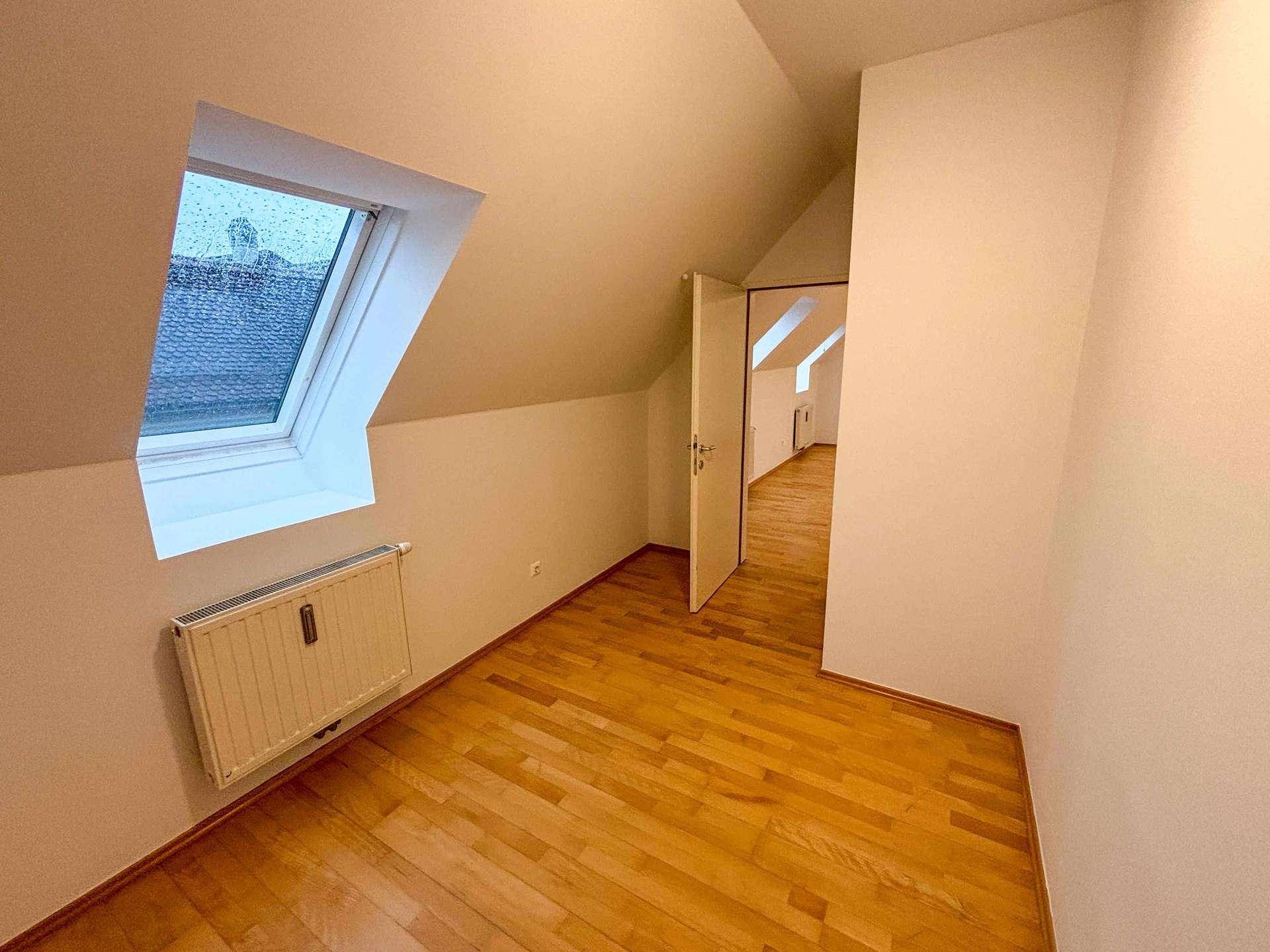 Dachgeschosszimmer mit Holzboden, Dachfenster und Zugang zu einem weiteren Raum.