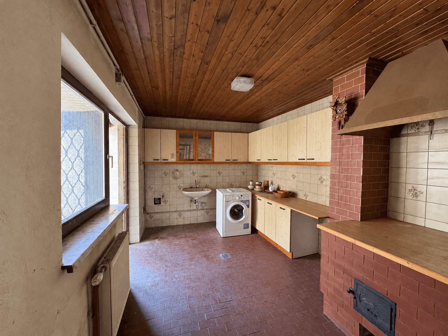 Hauswirtschaftsraum mit Waschmaschine, Fliesenboden und traditionellem Holzofen.