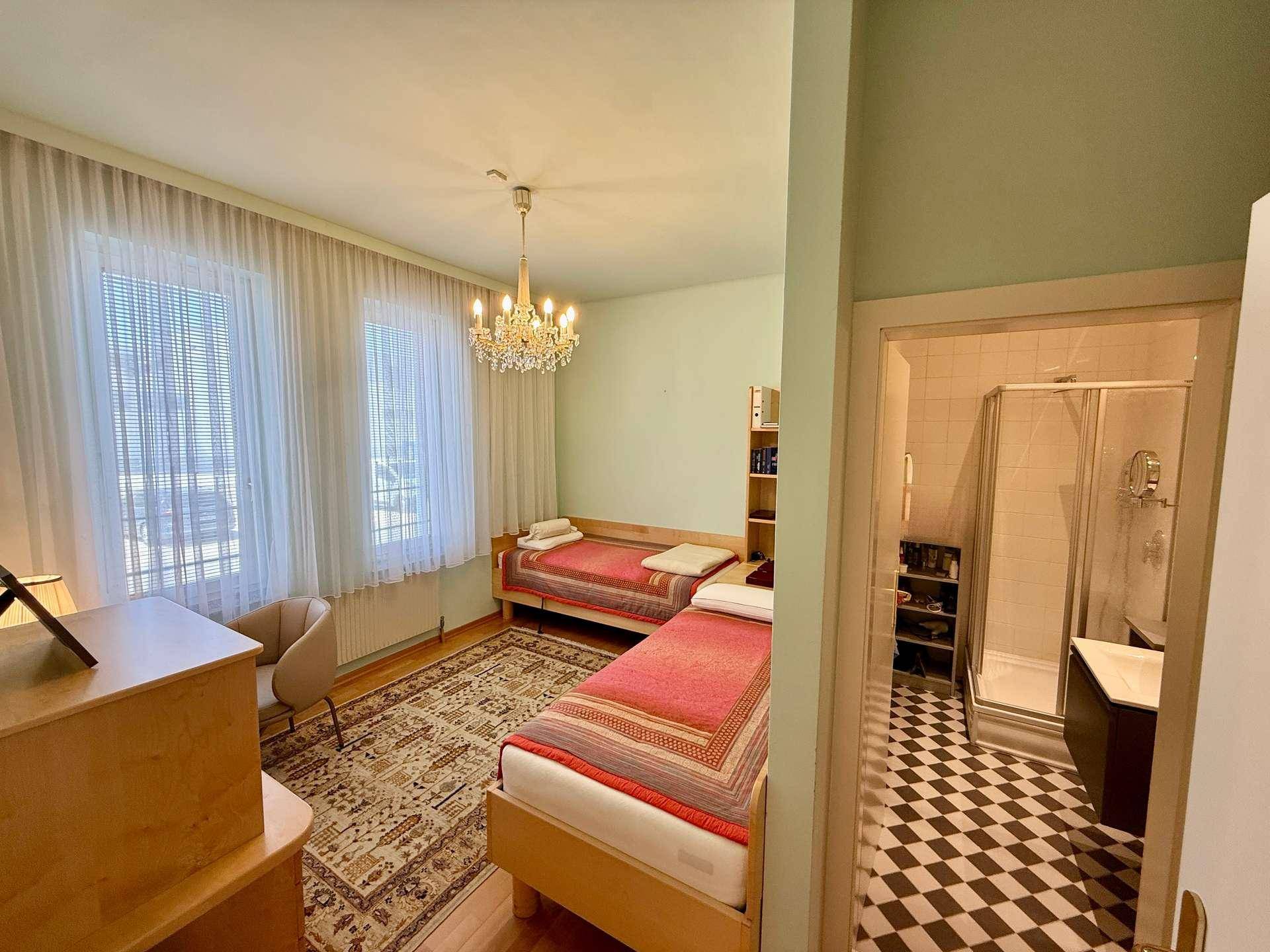 Schlafzimmer mit zwei Einzelbetten, Parkettboden und direktem Zugang zum Duschbad.