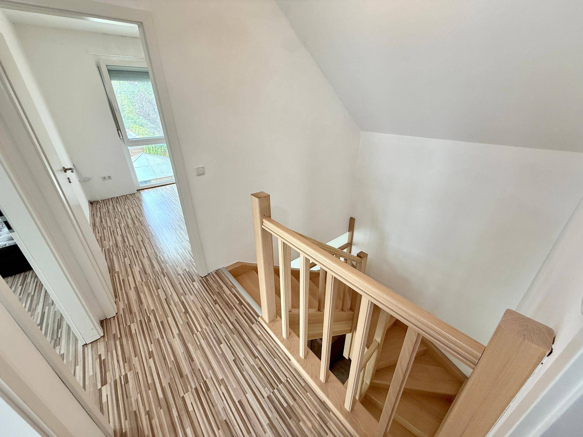 Heller Flur mit Holztreppe und Laminatboden, der zu den oberen Zimmern führt.