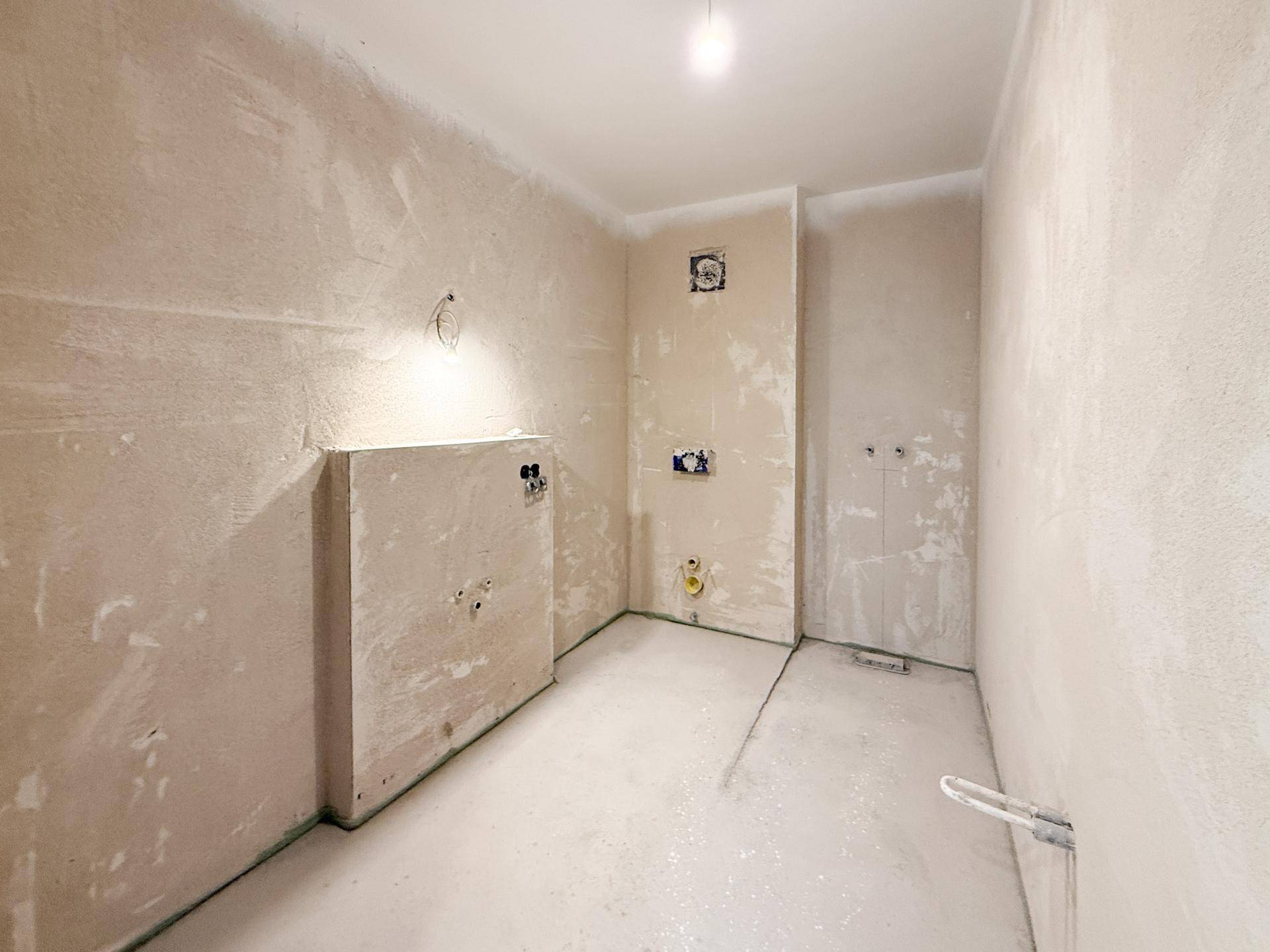 Badezimmer im Rohbauzustand mit vorbereiteten Wasseranschlüssen und Wänden.