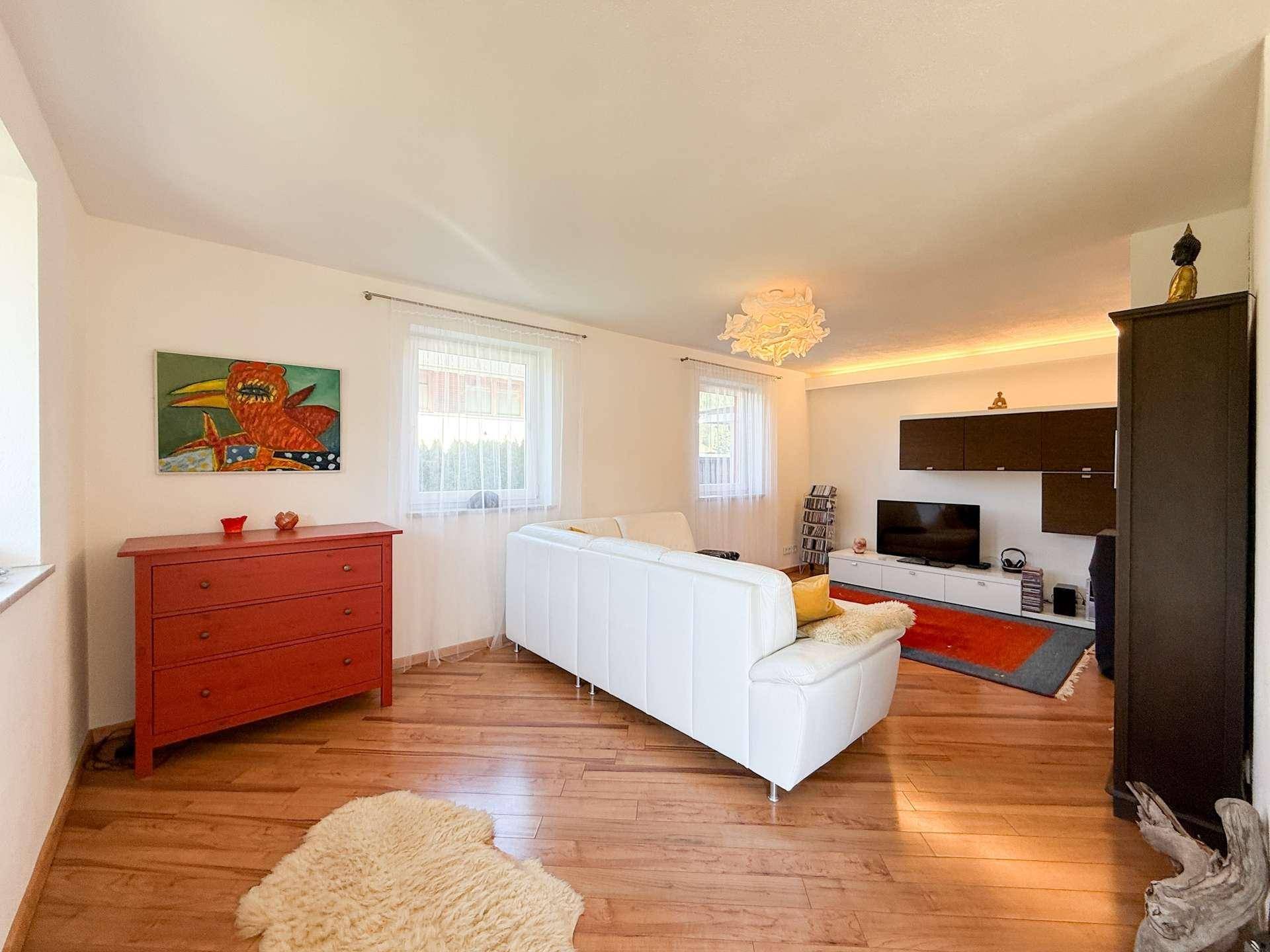 Heller Wohnbereich mit Holzboden, weißem Sofa und farbenfroher Dekoration.