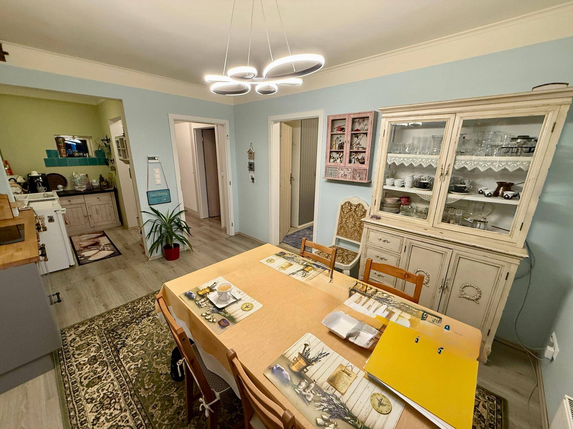 Essbereich mit großem Holztisch, Vitrinenschrank und Blick in die angrenzende Küche.
