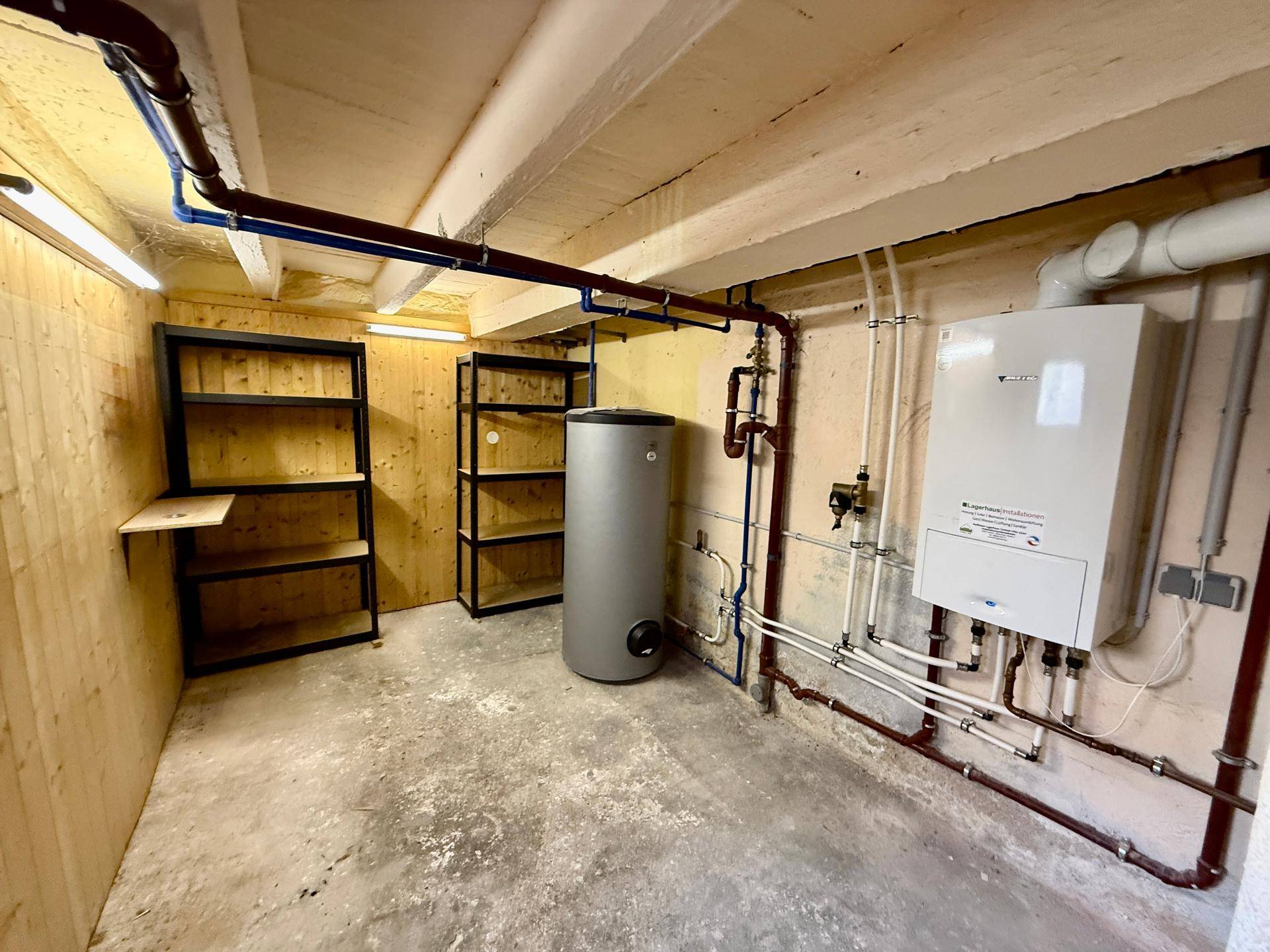 Heizungsraum mit Warmwasserspeicher, Heizkessel und Regalen für Lagerzwecke.