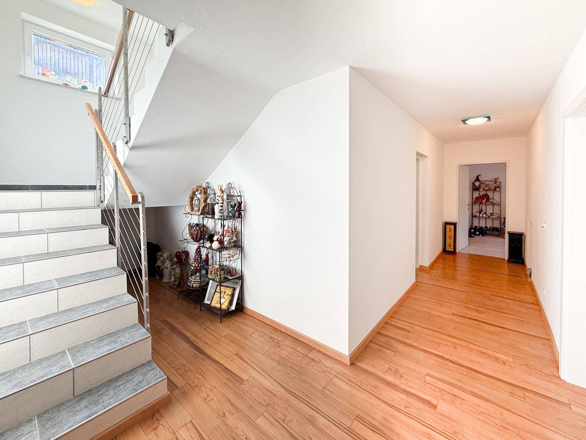 Heller Flur mit Treppe, Holzboden und dekorativen Elementen.