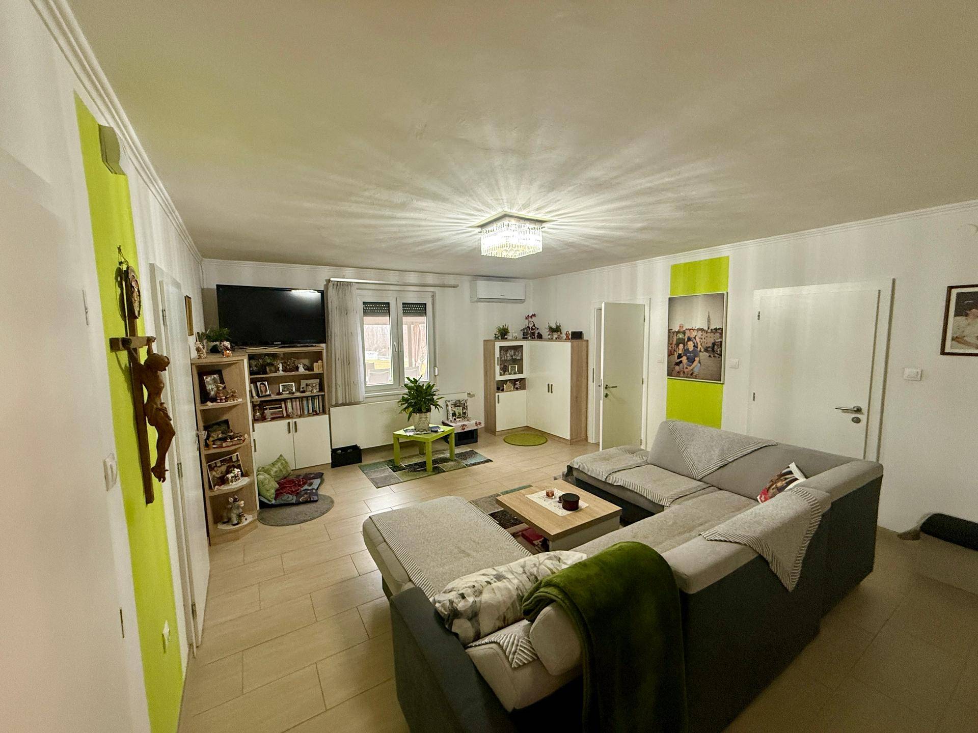 Gemütliches Wohnzimmer mit großem Ecksofa, Fernseher und grünen Akzenten.