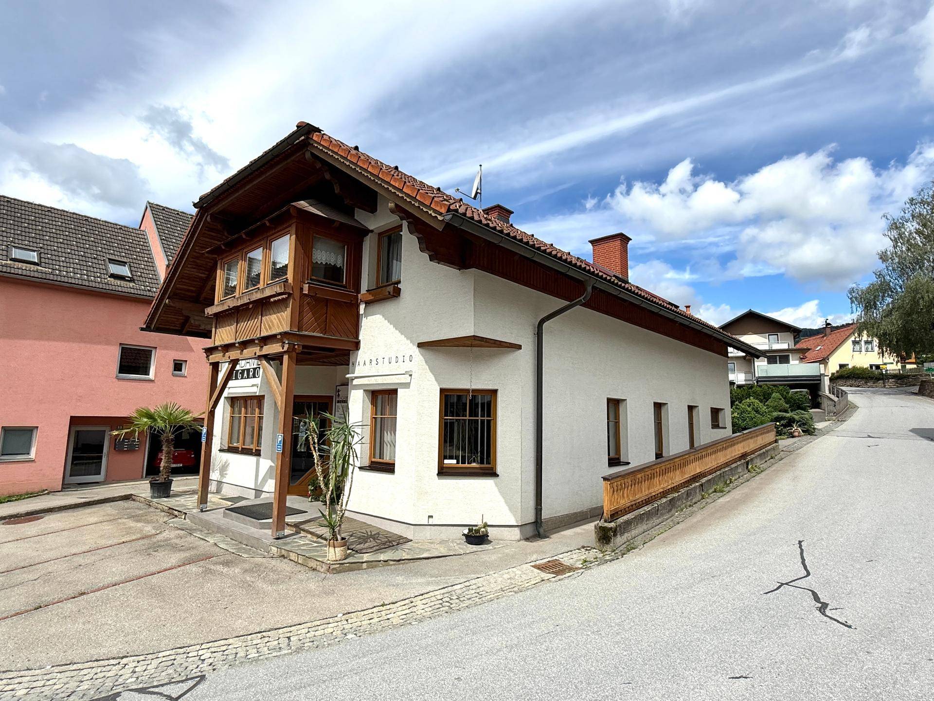 Seitenansicht des Hauses mit Erker und Hinweisschild für ein Haarstudio, umgeben von viel Grün.