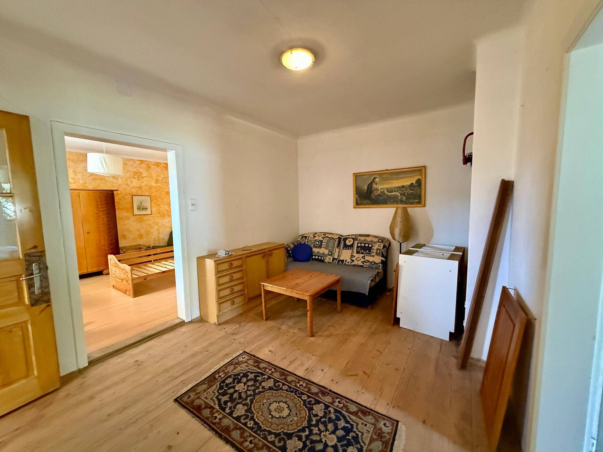 Gemütliches Wohnzimmer mit Holzboden, Sofa und traditionellem Teppich, bereit zur Einrichtung.