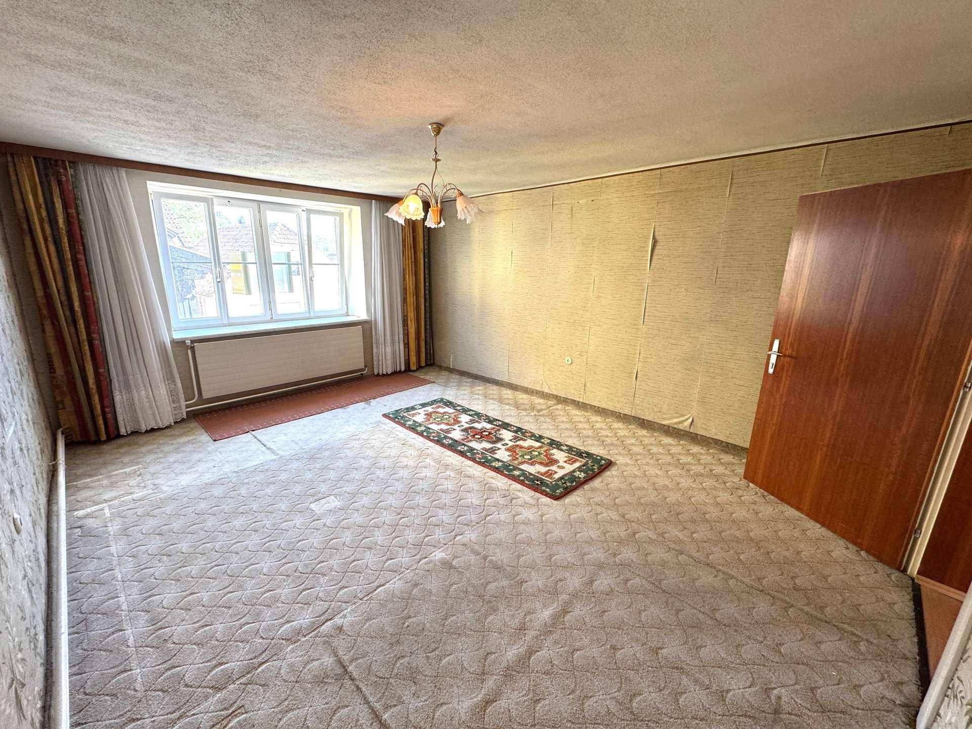 Schlafzimmer mit Teppichboden, großem Fenster und Tapeten in neutralen Farbtönen.