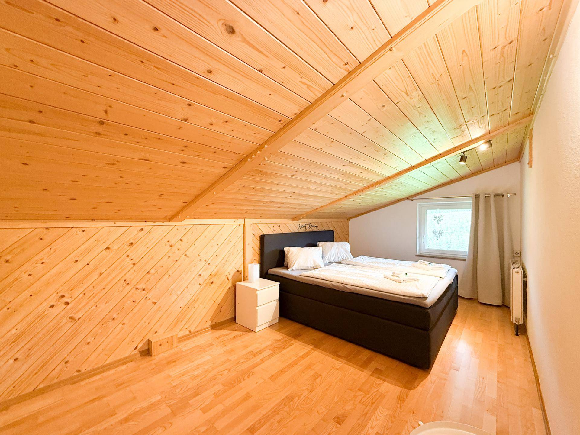 Gemütliches Schlafzimmer im Dachgeschoss mit Holzvertäfelung, Doppelbett und Holzboden.