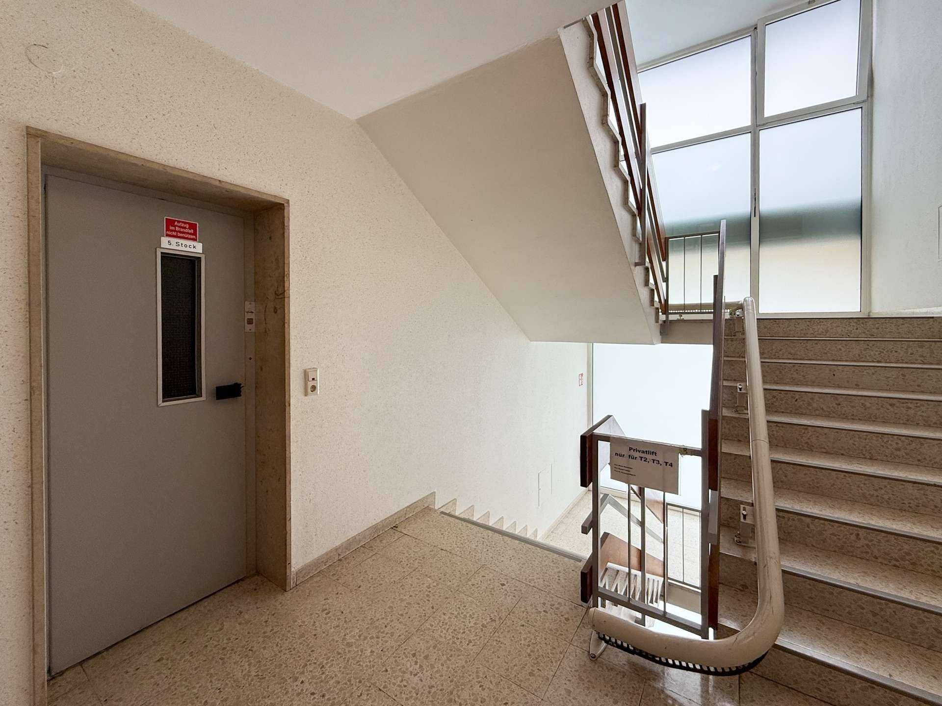 Heller Treppenaufgang mit Terrazzoboden und Zugang zum Aufzug im Mehrfamilienhaus.