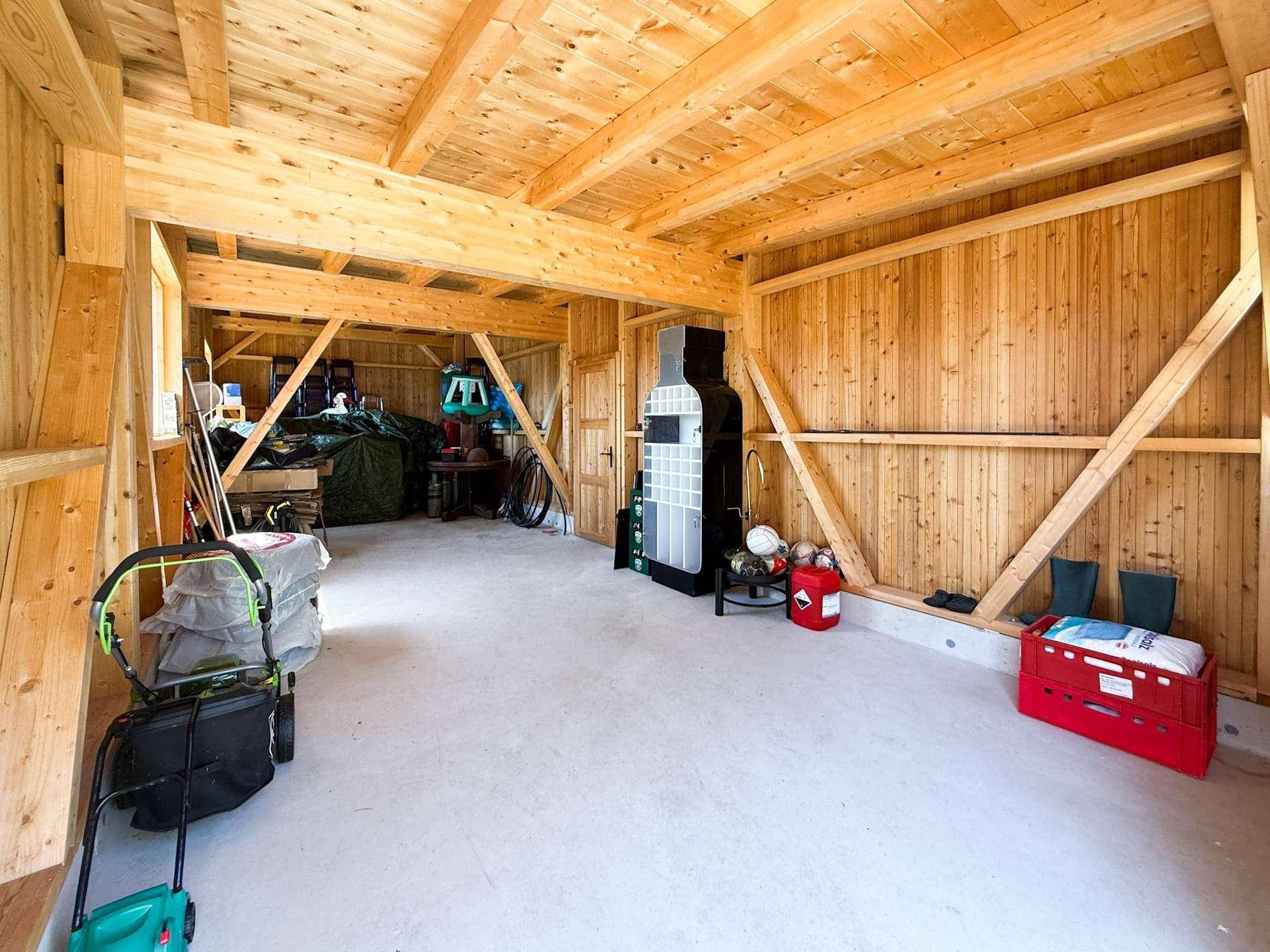 Großer Abstellraum im Holzgebäude mit Betonboden und viel Stauraum.