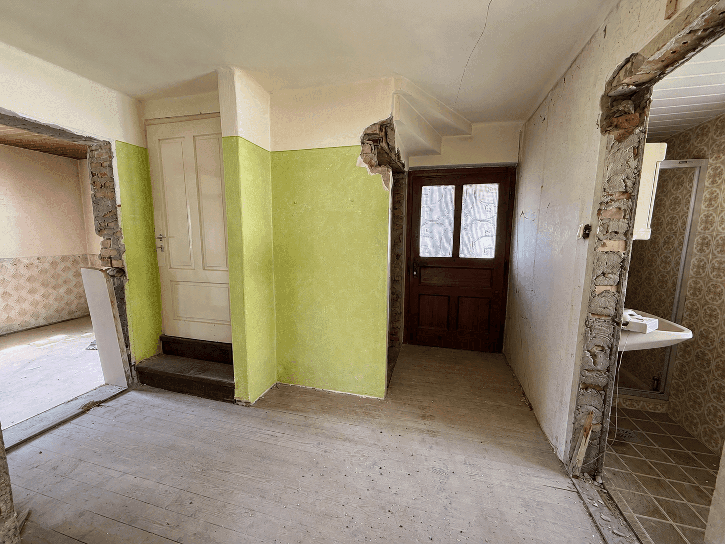 Innenraum im Umbau mit abgerissenen Wänden, alten Türen und sichtbaren Bauarbeiten.