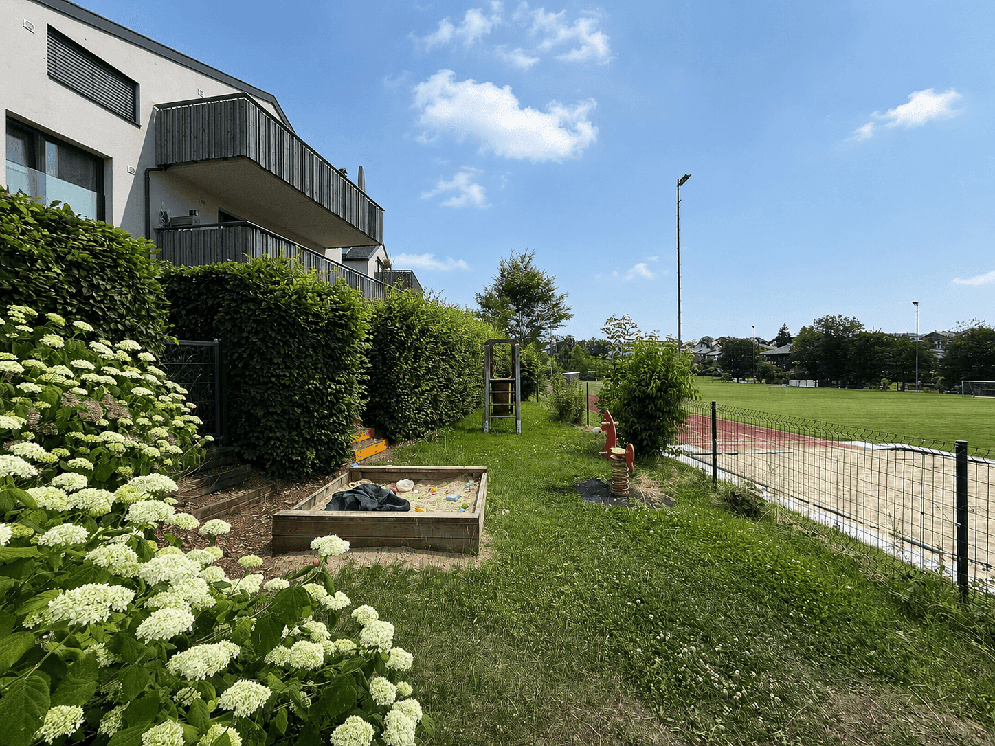 Gartenbereich mit Sandkasten und Spielgeräten neben dem Wohngebäude.