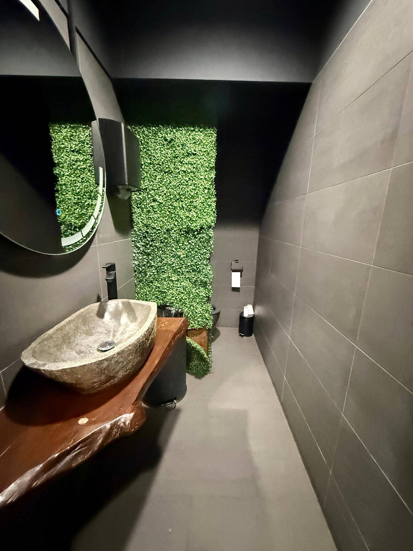 Modernes Badezimmer mit Steinswaschbecken auf Holzplatte und einer grünen Wandverkleidung.