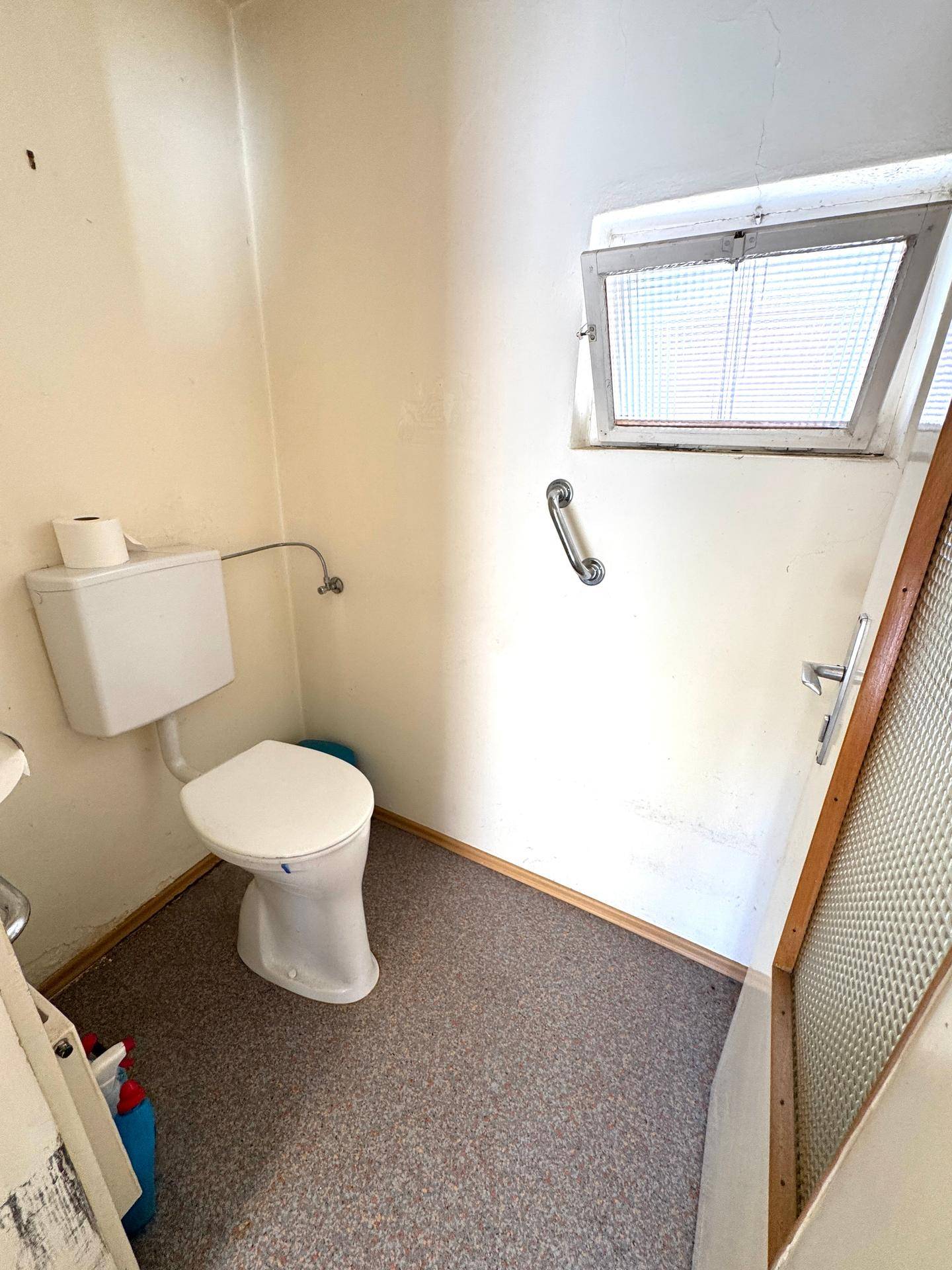 Kleines WC mit Fenster, einfacher Toilette und Haltegriff an der Wand.