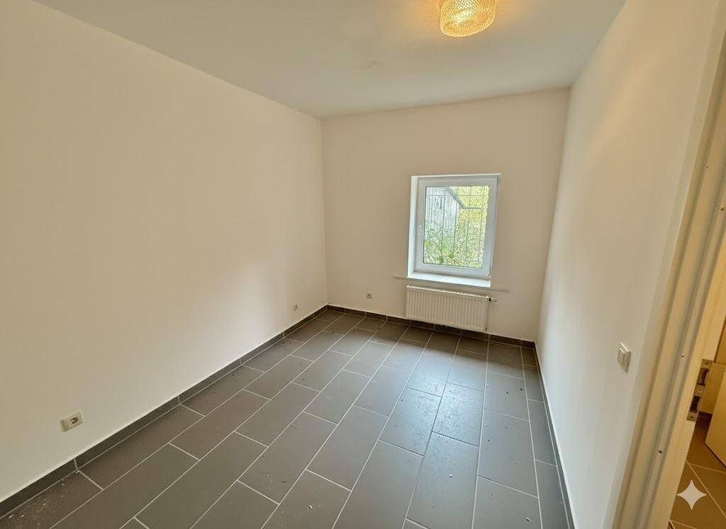 Leeres Zimmer mit grauen Fliesen und einem Fenster, geeignet als Schlaf- oder Arbeitszimmer.