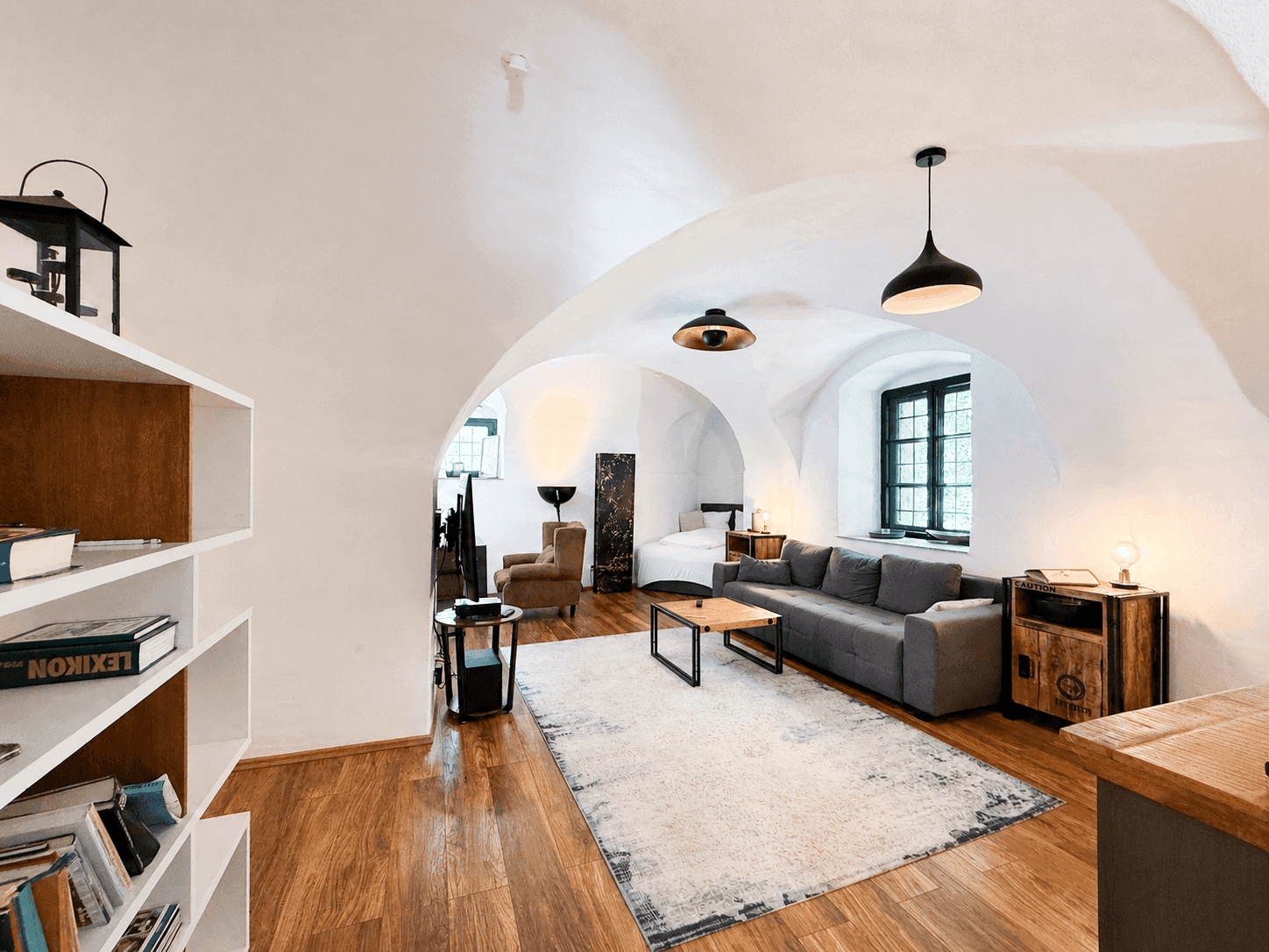Stilvolles Wohnzimmer mit Gewölbedecken, Holzboden und einem Bücherregal als Raumteiler.
