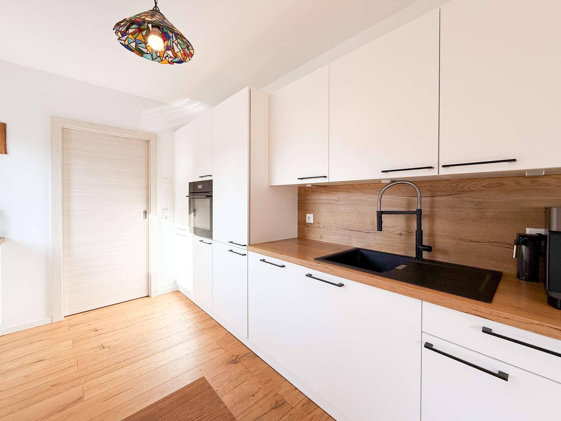 Stilvolle Küche mit weißen Schränken, Holz-Rückwand und schwarzer Spüle.