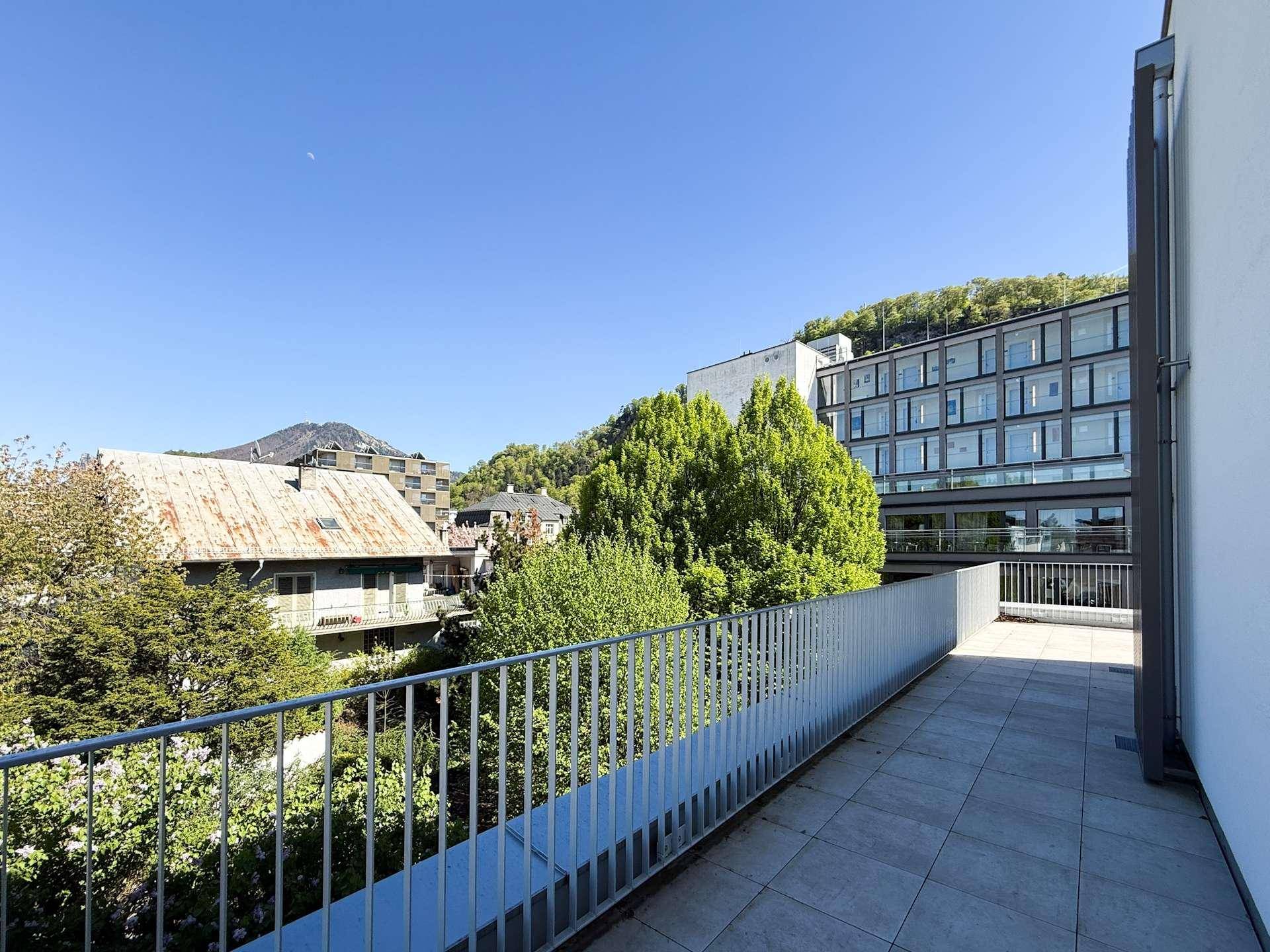 Terrasse mit weitem Blick über die grüne Umgebung und angrenzende moderne Gebäude.