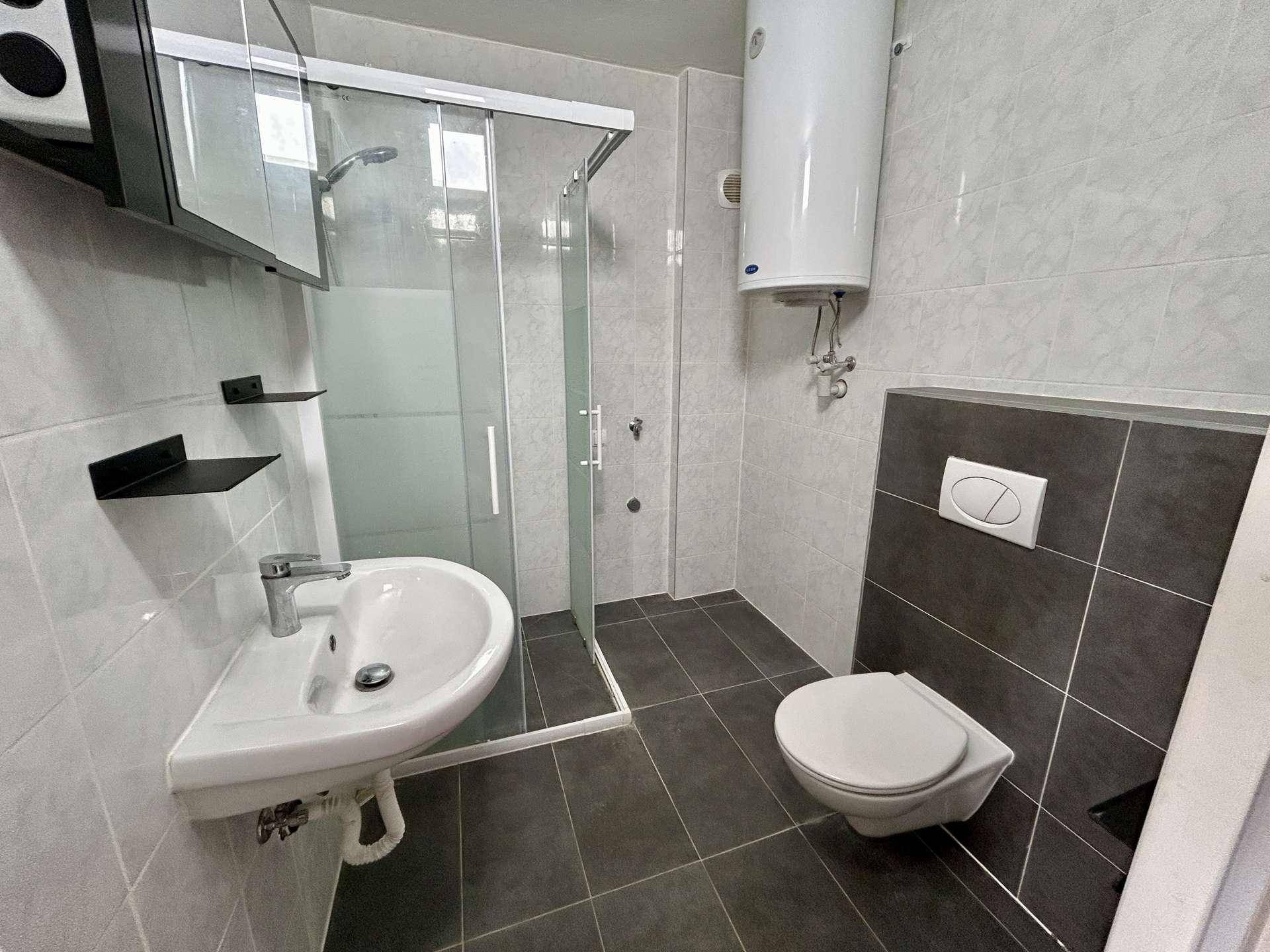 Modernes Badezimmer mit Duschkabine, wandhängendem WC und grauen Fliesen.