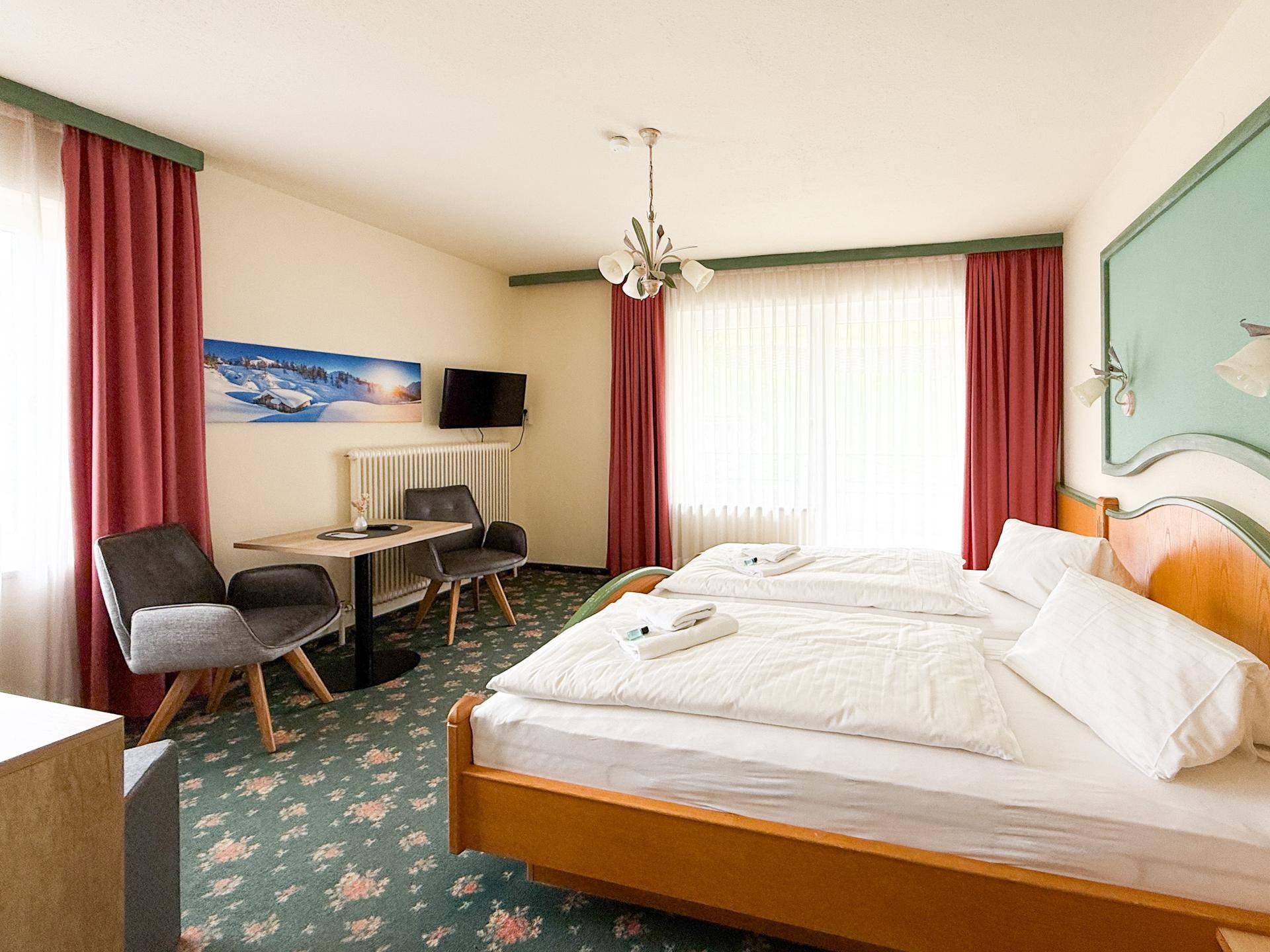 Komfortables Schlafzimmer mit Doppelbett, Teppichboden und einem kleinen Sitzbereich am Fenster.